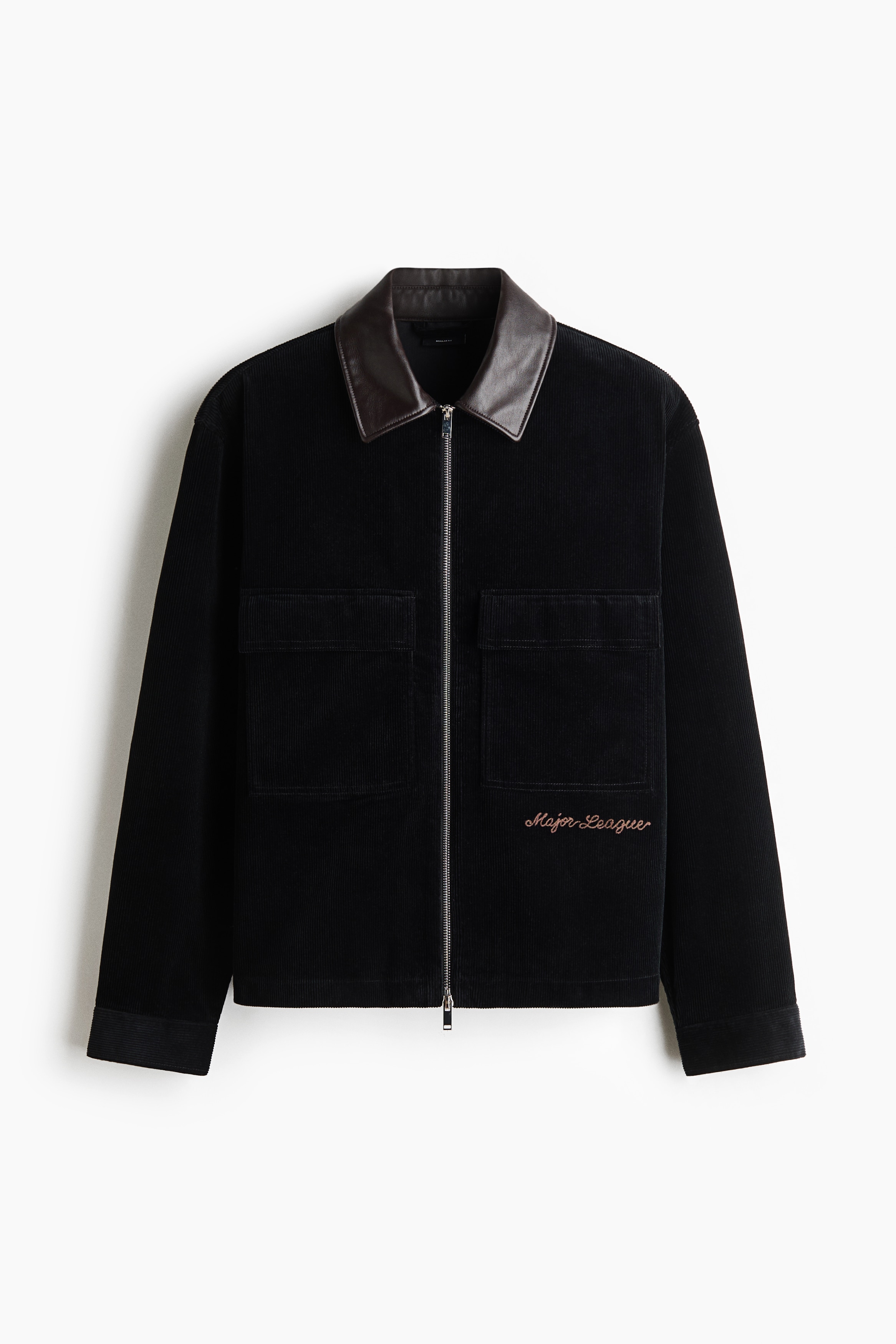 Eine schwarze Cordjacke mit kontrastierendem braunem Lederkragen wird vom Model Ã¼ber einem grauen T-Shirt und dunklen Hosen getragen. Die Jacke verfÃ¼gt Ã¼ber einen silberfarbenen Frontreissverschluss, grosse aufgesetzte Brusttaschen mit Patten und eine aufgestickte Schriftzug-Details auf der linken unteren Seite.