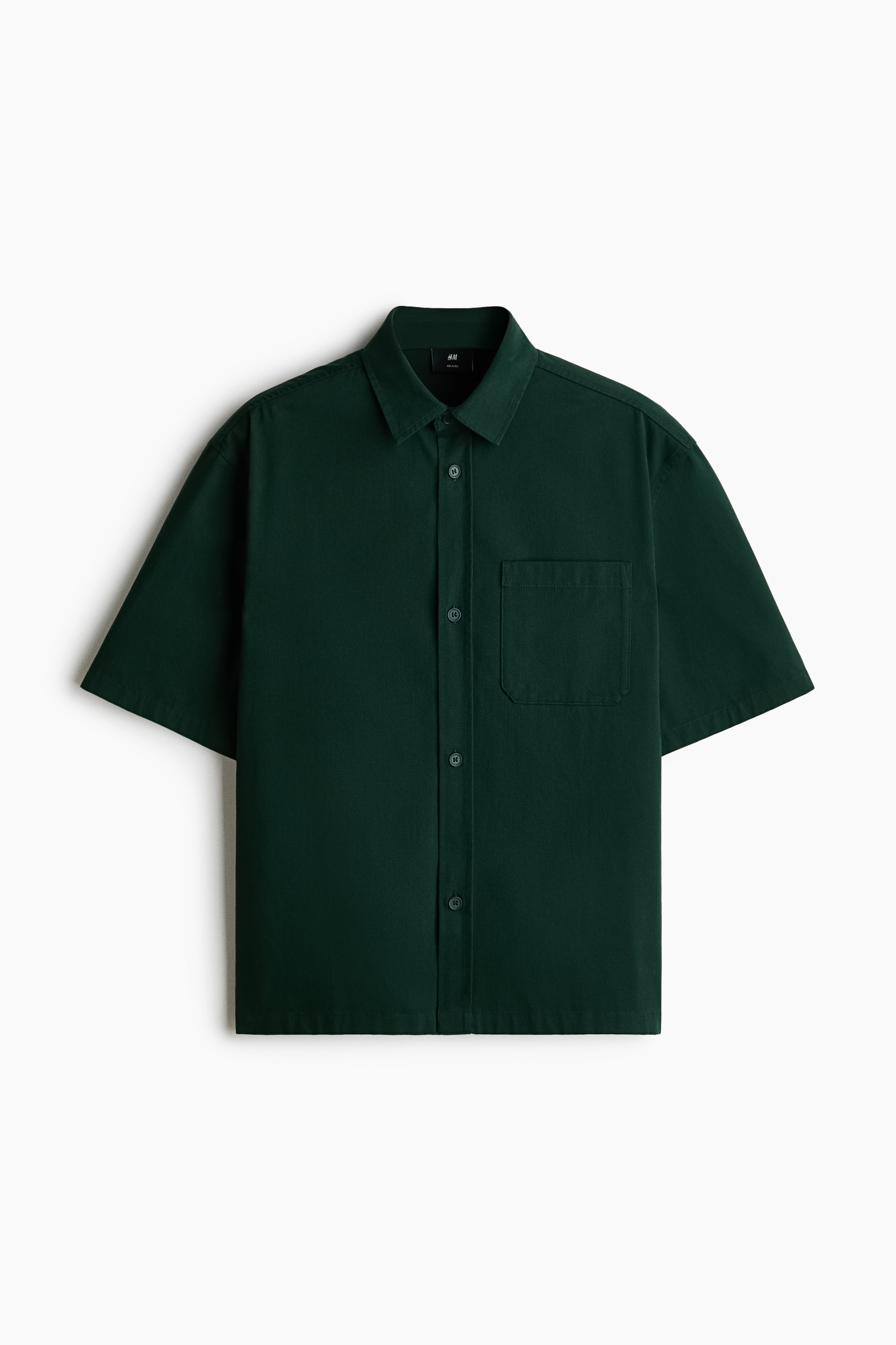 Voir une image plus grande: Une chemise en sergé de coton vert foncé affiche son devant, avec un col classique, une patte de boutonnage, des manches courtes et une poche poitrine ouverte sur la gauche. Elle présente un ourlet droit et une coupe décontractée.
