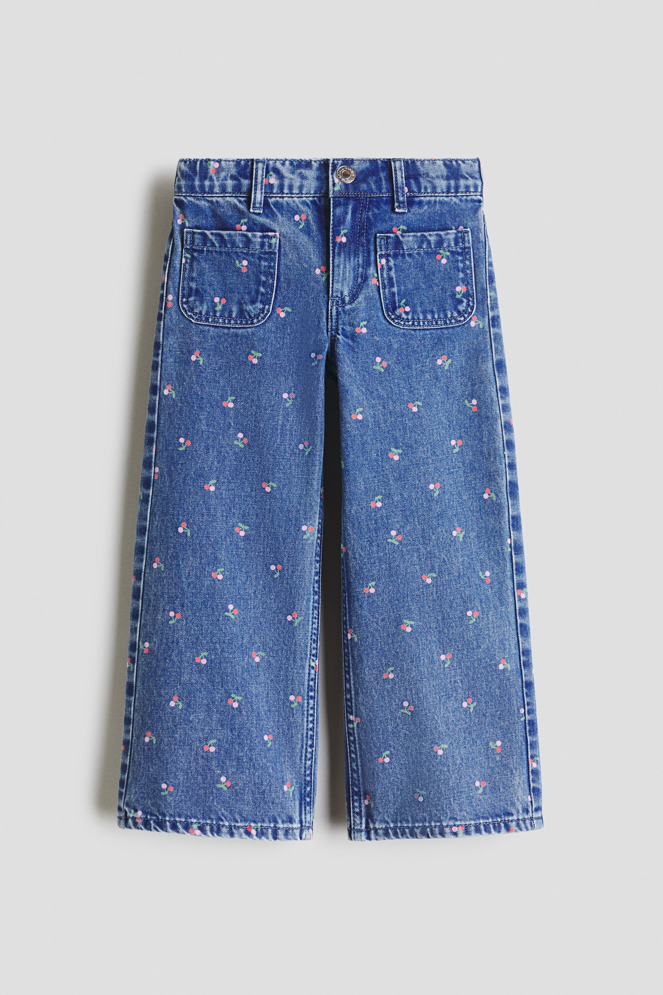 View larger image: Blue denim jeans are showcased in a front view, displaying an all-over pattern of small pink and red cherries with green stems. They feature a wide-leg cut, a front button and zip fastening, and two rounded patch pockets on the upper front.