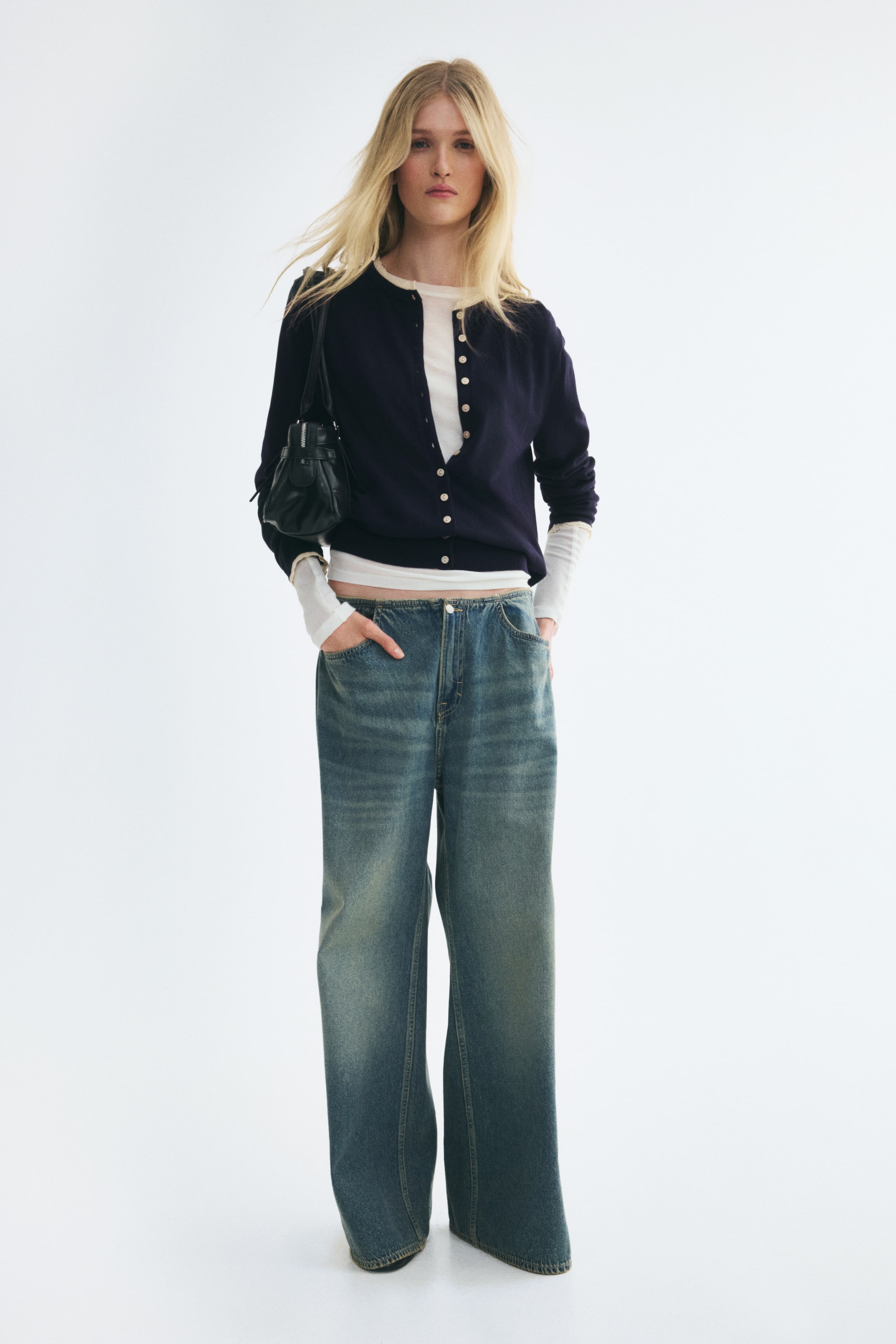 View larger image: A navy blue long-sleeve cardigan, shown from the front, features a round neckline, a button-down front, and delicate lace trim details at the neckline and cuffs. The cardigan is layered over a white long-sleeve top and styled with wide-leg blue jeans, highlighting its ribbed neckline, cuffs, and hem.