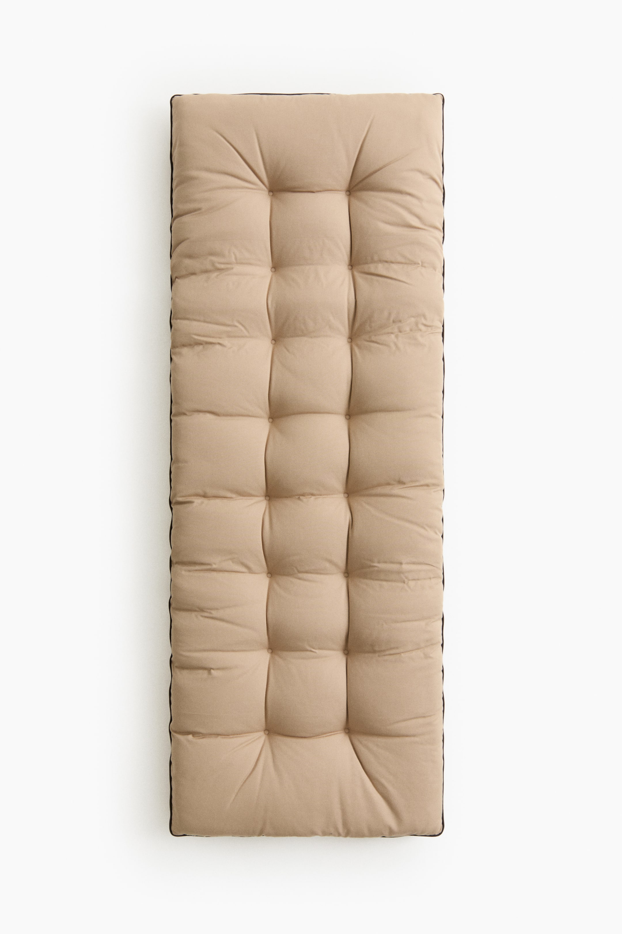 Visa större bild: En lång, rektangulär beige tuftad kudde visar sin framsida. Den har fyrkantiga quiltade sektioner över hela ytan, och mörka kanter syns längs dess sidor.