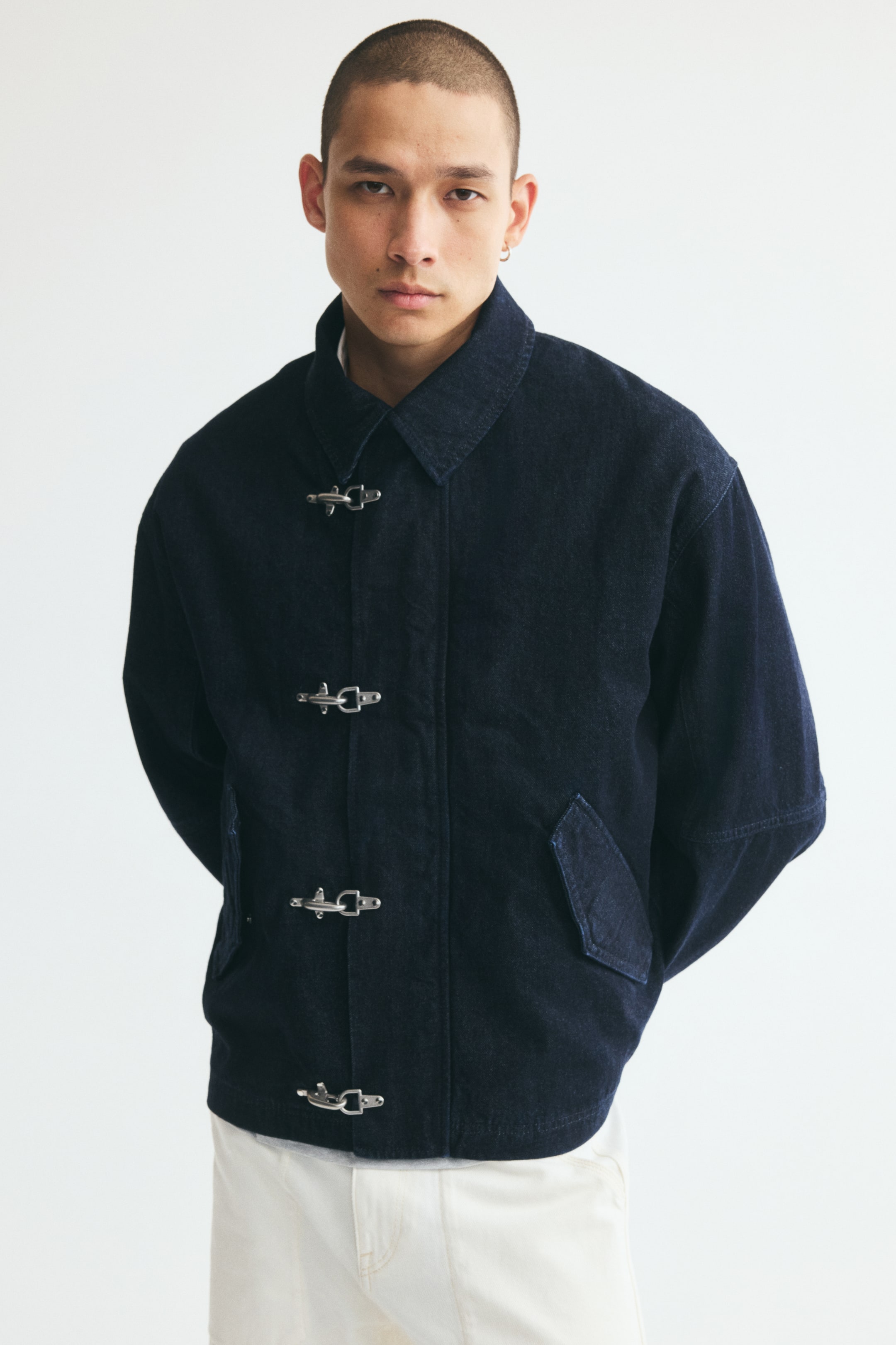 Visualizza immagine più grande: La modella indossa una giacca in denim di cotone blu scuro. La giacca presenta un colletto classico, quattro fermagli metallici argentati sul davanti e tasche con patta oblique.