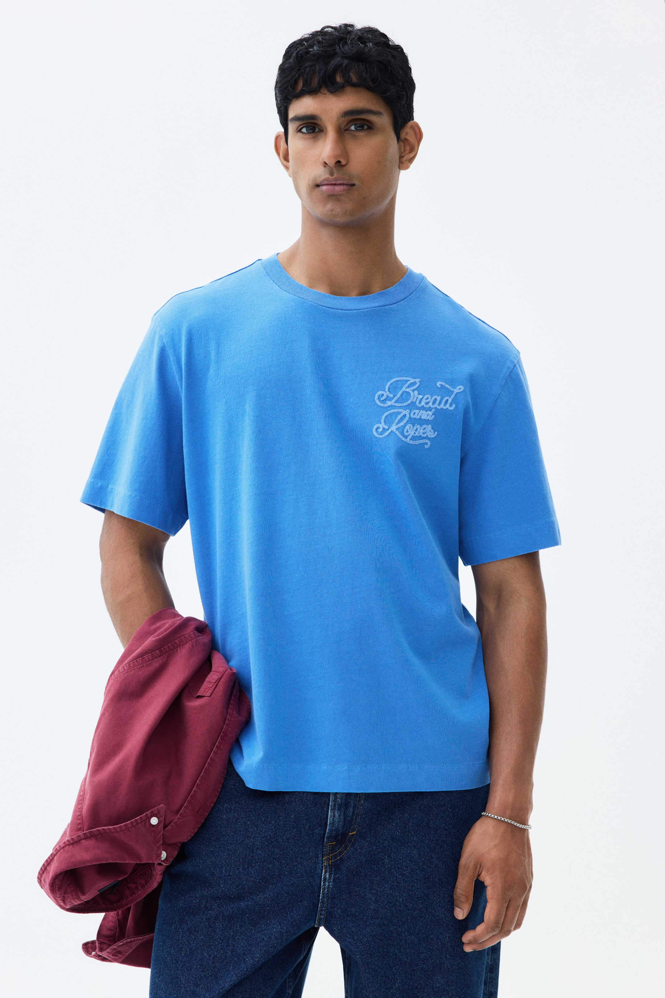 View larger image: The model is showcasing a blue T-shirt crafted from heavyweight cotton jersey. It features a light blue embroidered 'Bread and Ropes' motif on the left chest. The design includes a round rib-trimmed neckline, dropped shoulders, a straight-cut hem, and offers a regular fit.