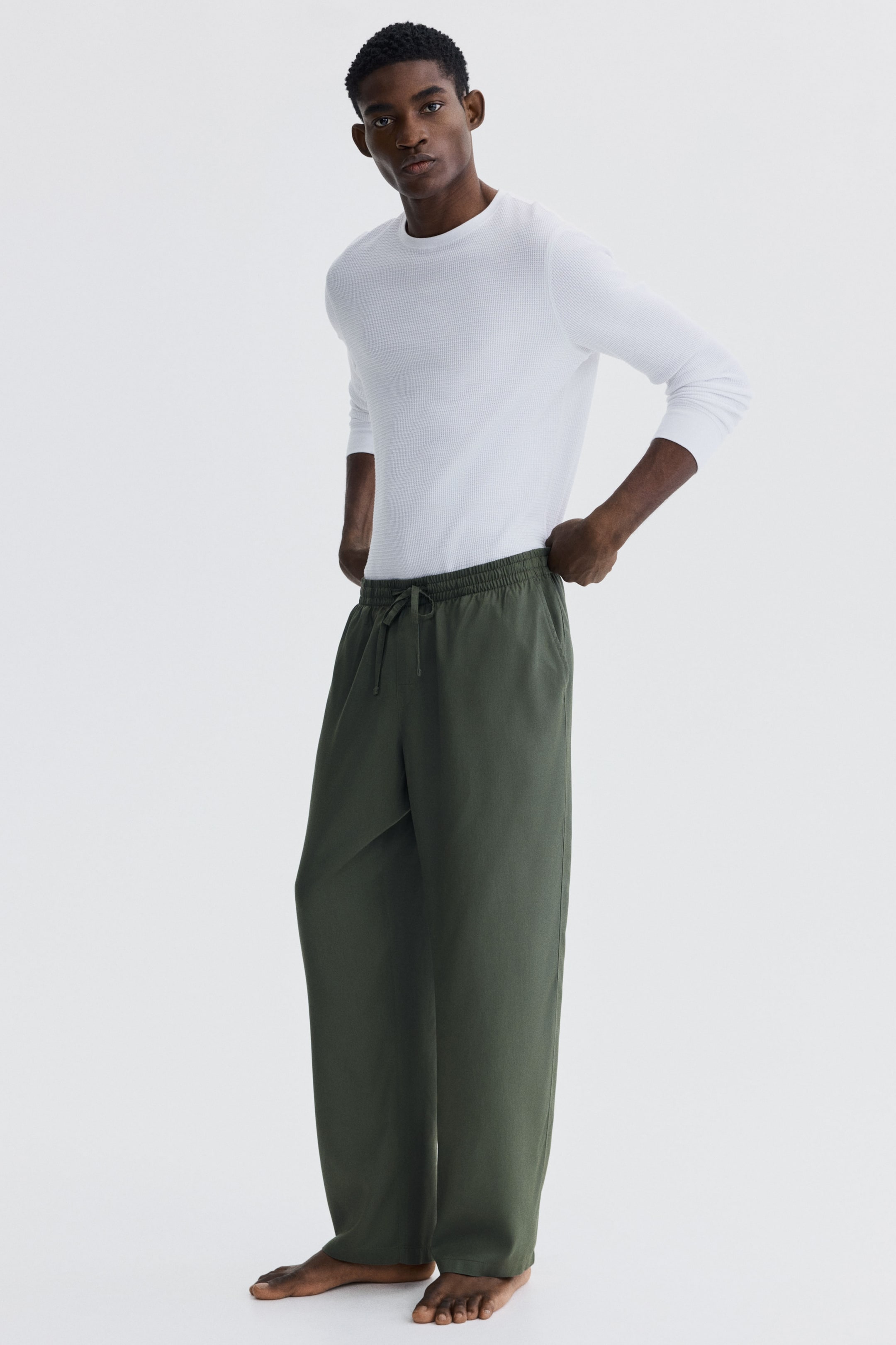 Agrandir l'image: Pantalon vert foncé à coupe décontractée présenté sous un léger angle avant-gauche, doté d'une taille élastiquée avec cordon de serrage, de poches latérales et d'une jambe large tombant librement jusqu'aux chevilles.