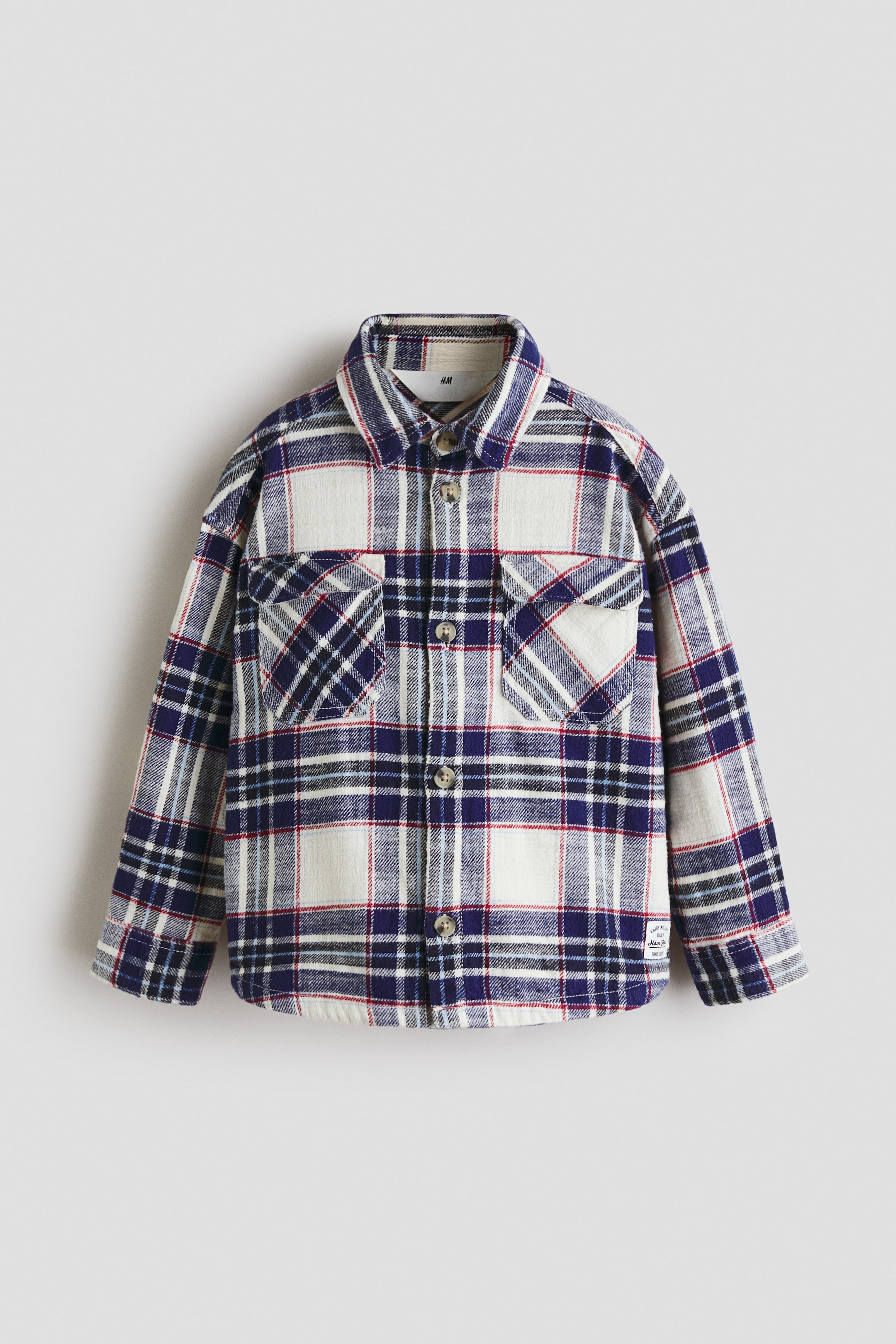 View larger image: An oversized shirt is showcasing its front, featuring a blue, white, and red check pattern. It displays a collar, buttons down the front, dropped shoulders, long sleeves with buttoned cuffs, and two flap chest pockets.
