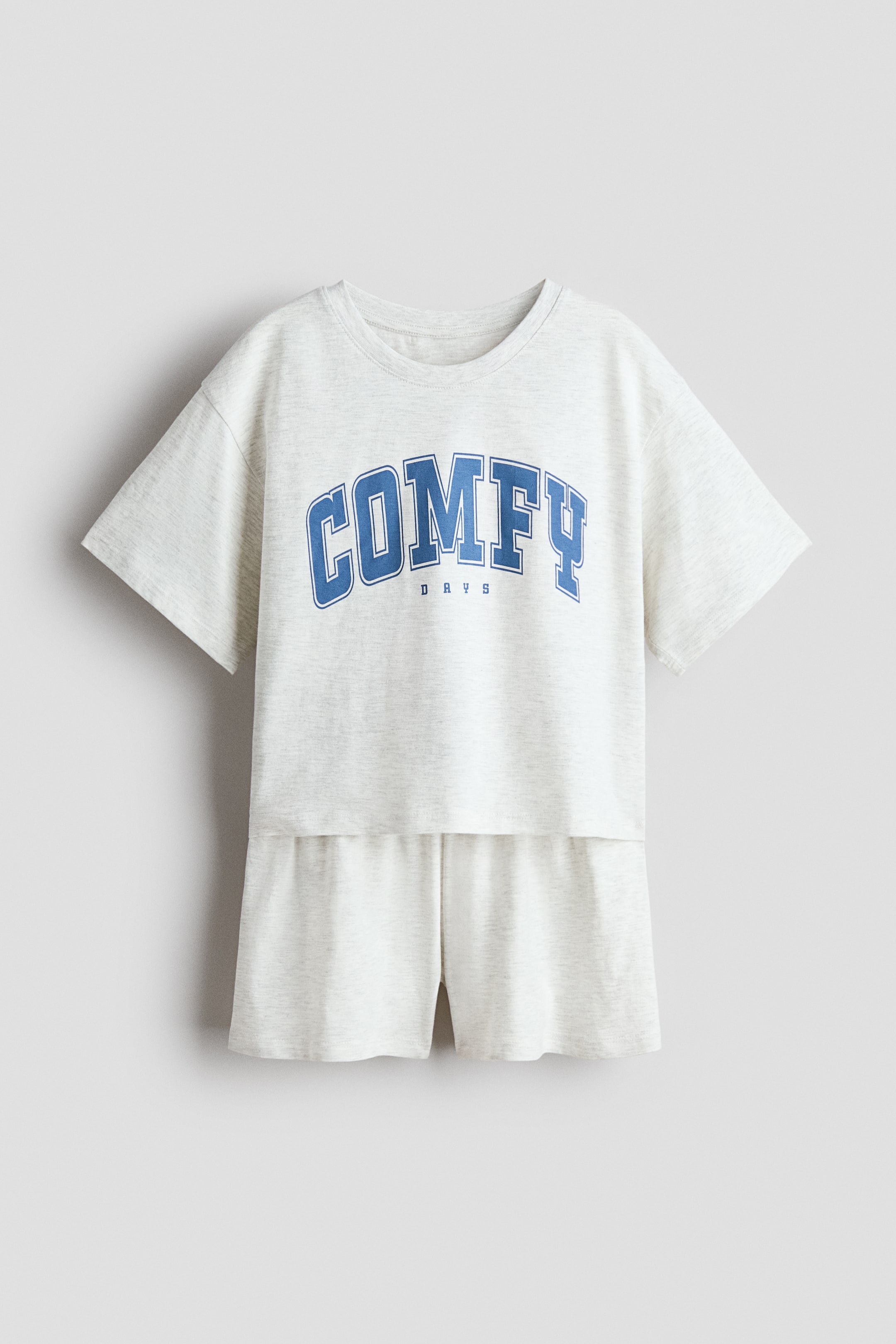 View larger image: A pyjama set in light grey marl cotton jersey, featuring a T-shirt-style top with a round neckline, dropped shoulders and short sleeves, with 'COMFY DAYS' in blue arched lettering across the front. The matching shorts have an elasticated waist.