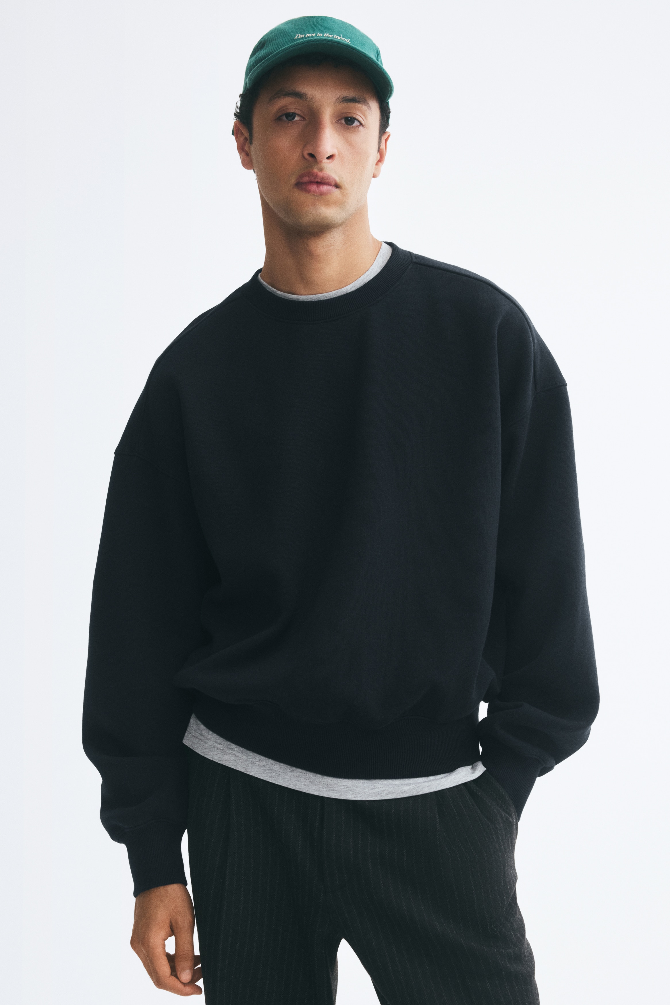 A black crewneck sweatshirt displays a relaxed fit with dropped shoulders and long, full sleeves. The sweatshirt features a ribbed neckline, ribbed cuffs, and a matching ribbed hemline in a direct front-facing view.