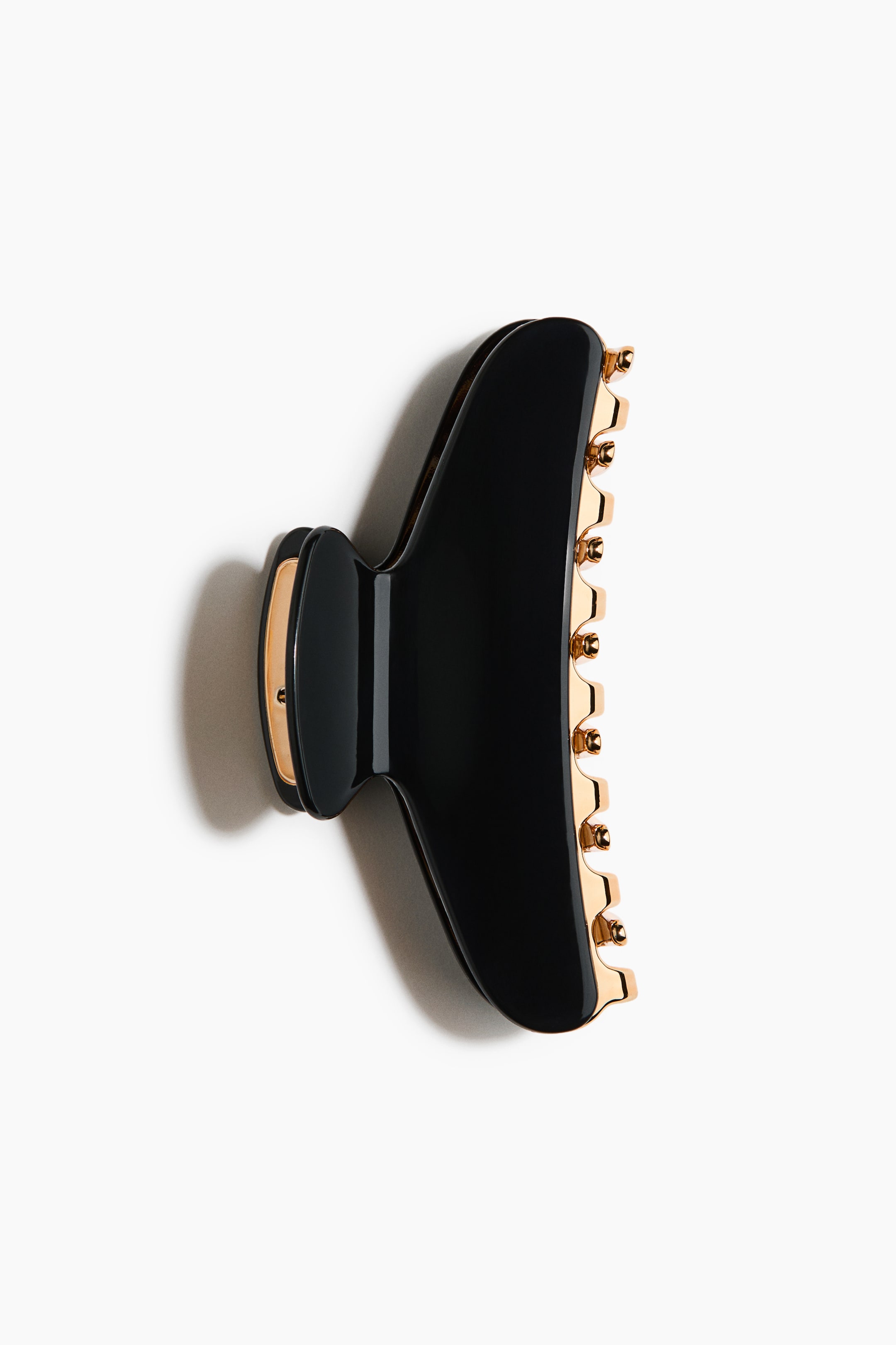 View larger image: A black hair claw clip is lying flat, facing right. It boasts a glossy finish with gold-toned teeth visible along its inner edge and gold accents on the hinge.