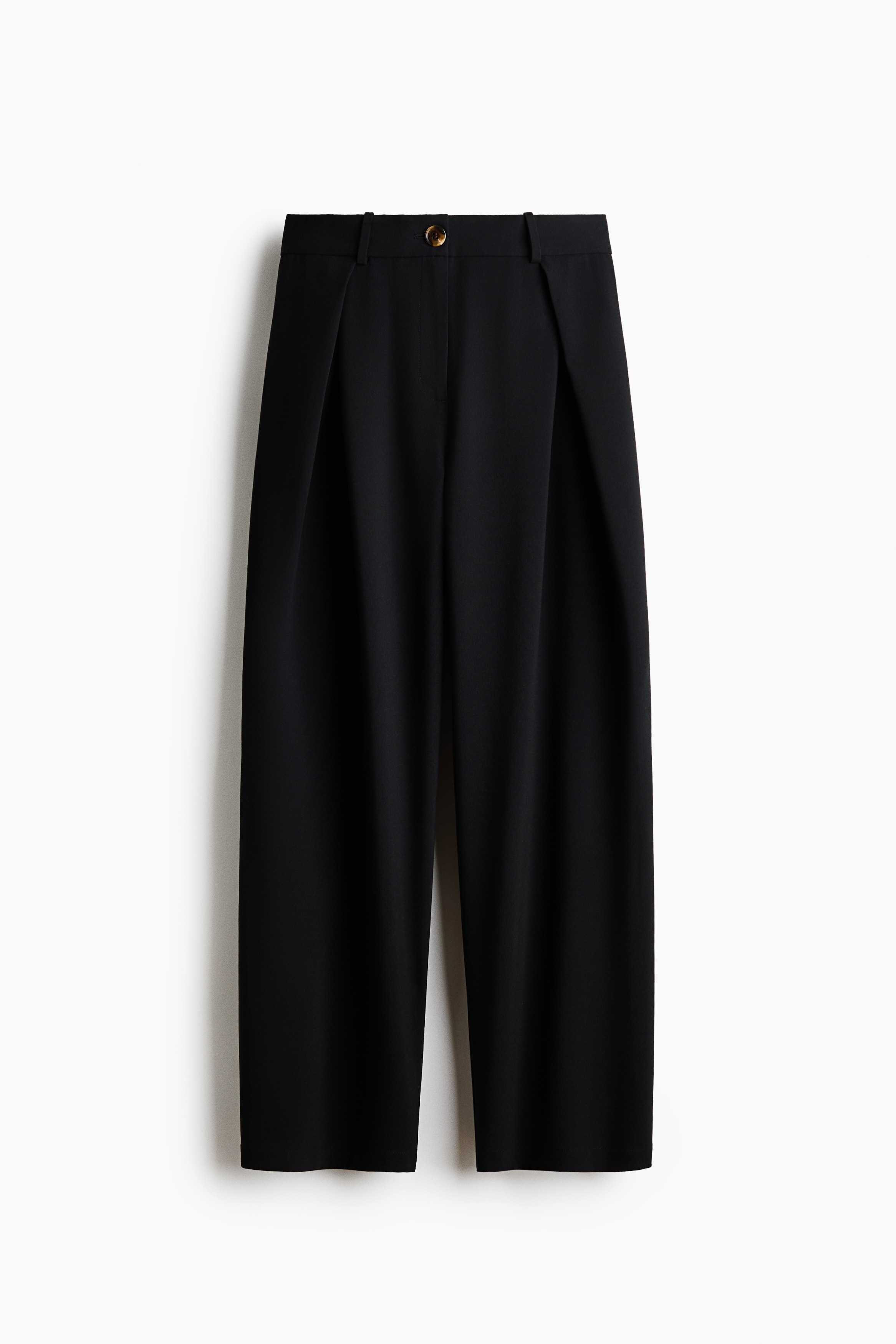 Skræddersyede bukser med brede ben, høj talje, knaplukning og læg foran bæres af modellen. De løstsiddende bukser styles med en mørk læderjakke.