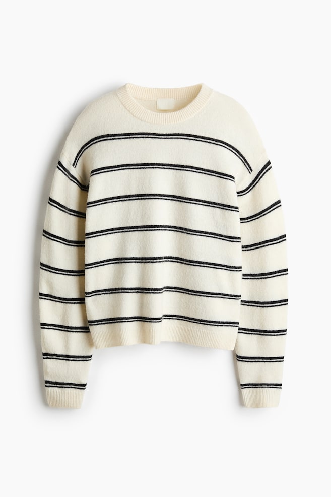 Se muestra un jersey de punto color crema desde el frente, con dos franjas negras horizontales que recorren el cuerpo y las mangas largas. El jersey presenta un cuello redondo con ribete de canalé, hombros caÃdos y remate de canalé en los puños y el bajo. - 1