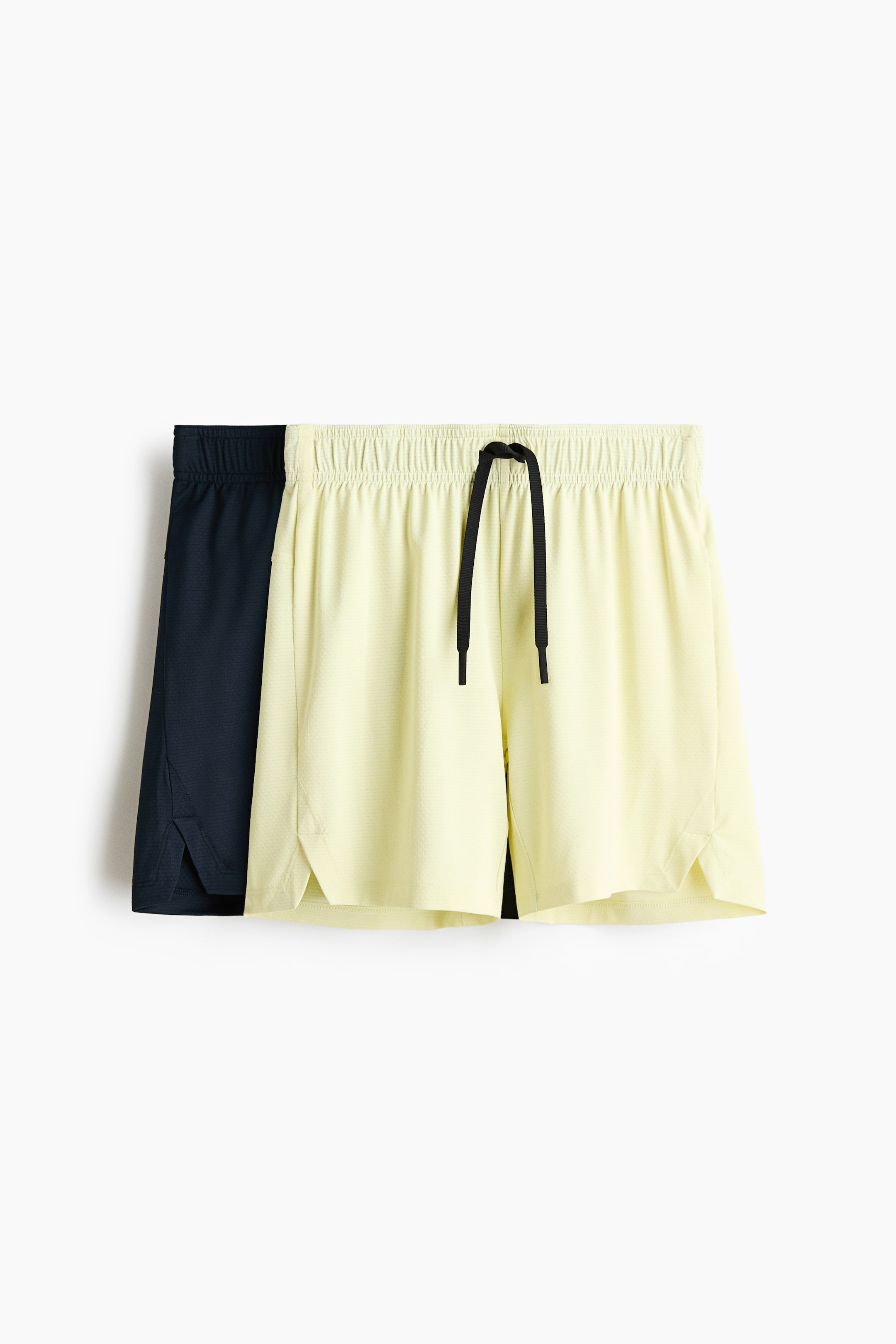 Преглед на по-голямо изображение: Два чифта спортни шорти са показани отпред, като светложълтият чифт частично припокрива тъмносиния чифт. Светложълтите шорти отпред са с еластична талия с черен шнур и прорезани отвори за краката, докато тъмносините шорти също са с прорезани отвори за краката.