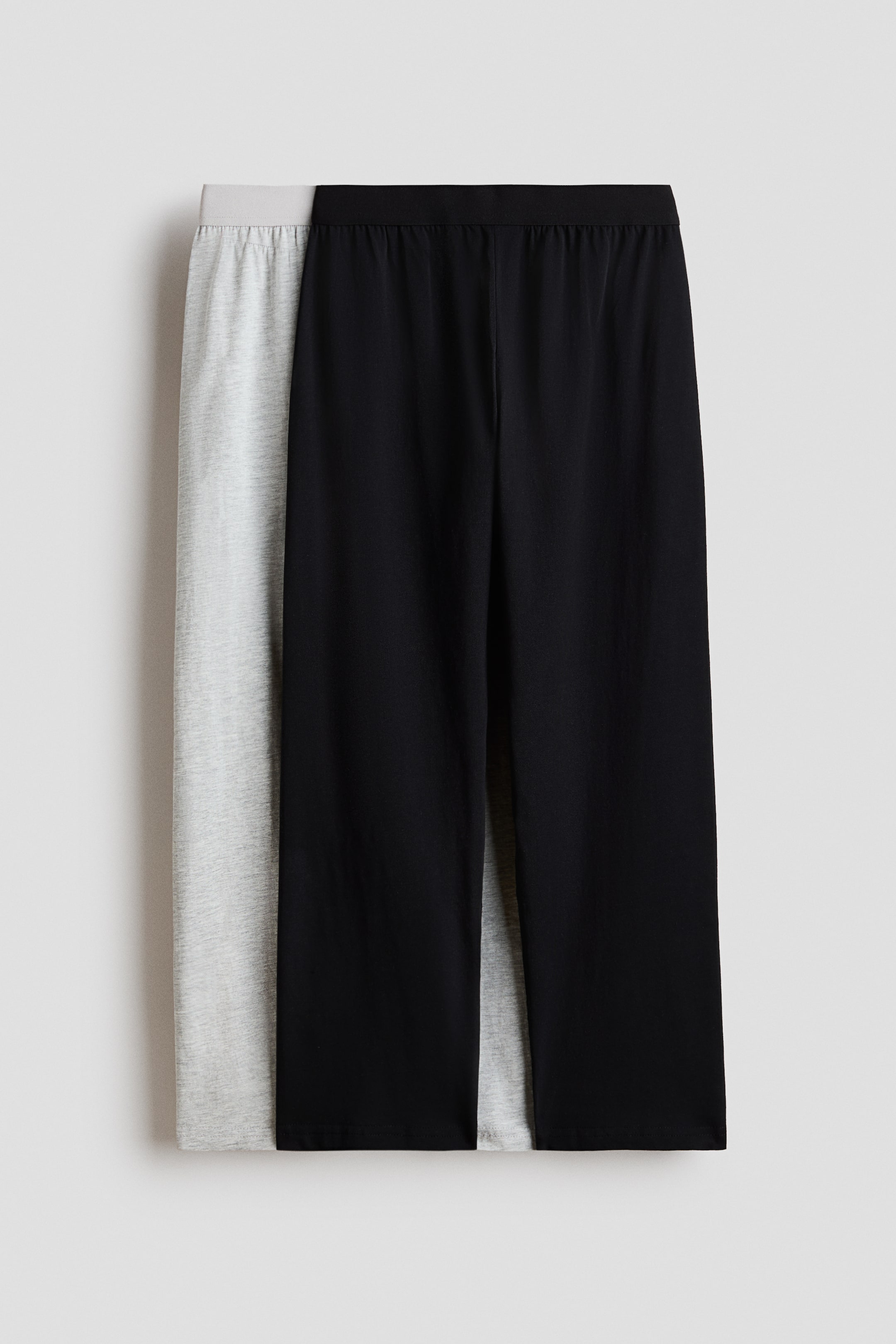 Größeres Bild ansehen: Eine schwarze Hose liegt teilweise über einer hellgrauen Hose. Die schwarze Hose verfügt über einen elastischen Bund und einen entspannten, geraden Schnitt.