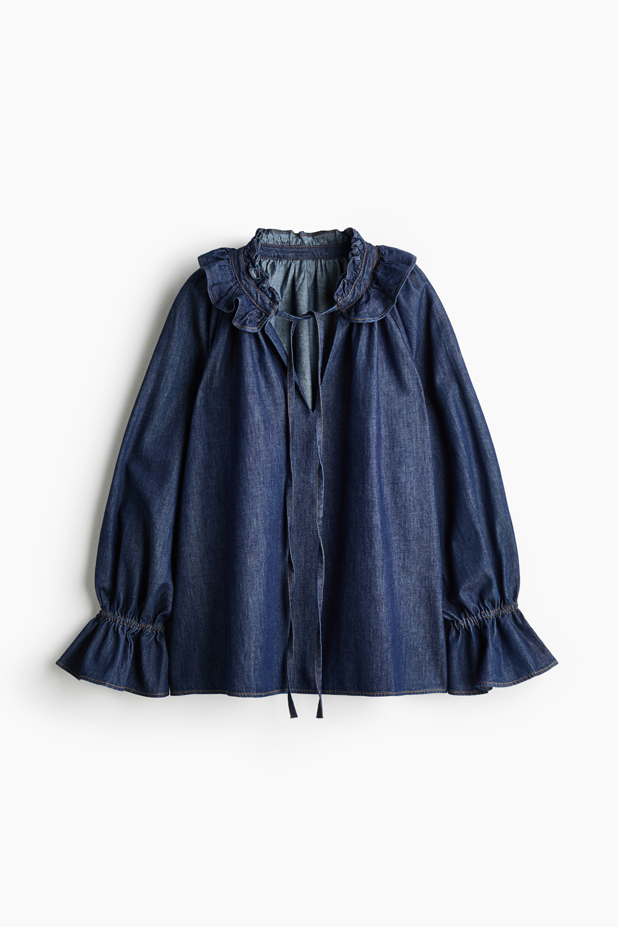 View larger image: A dark blue denim blouse is shown from the front, featuring a ruffled high collar with a V-neckline and slim, dangling tie closures. The blouse is designed with voluminous long sleeves that end in smocked, flared cuffs, creating a relaxed and flowy silhouette.