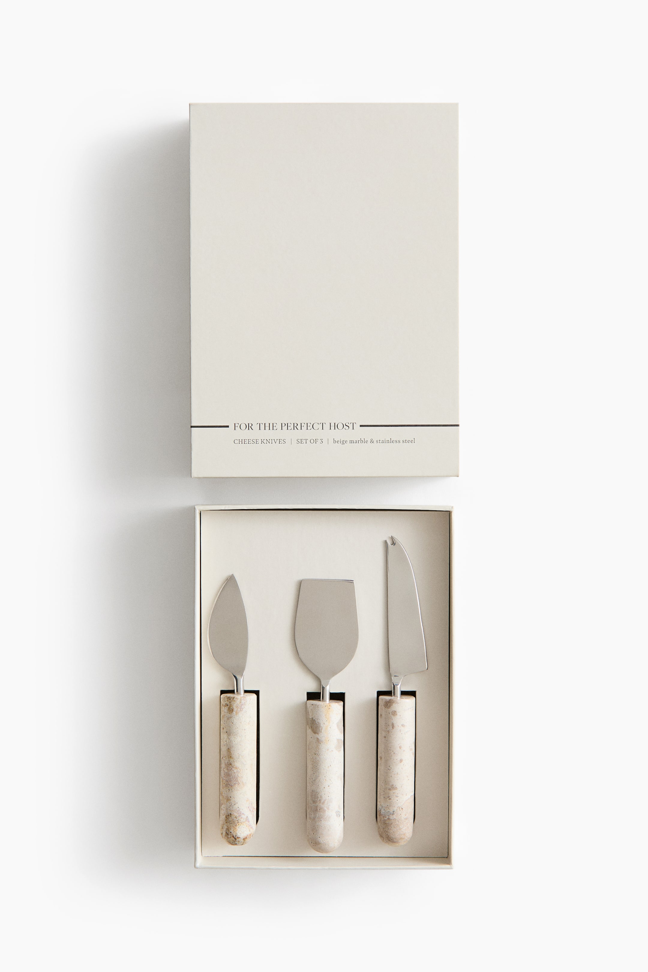 View larger image: A set of three cheese knives with cylindrical beige marble handles and stainless steel blades is resting facing front in a beige presentation box, with its matching lid displayed above. The set features a heart knife, a flat chisel knife, and a pronged serving knife neatly arranged in custom-fit slots.