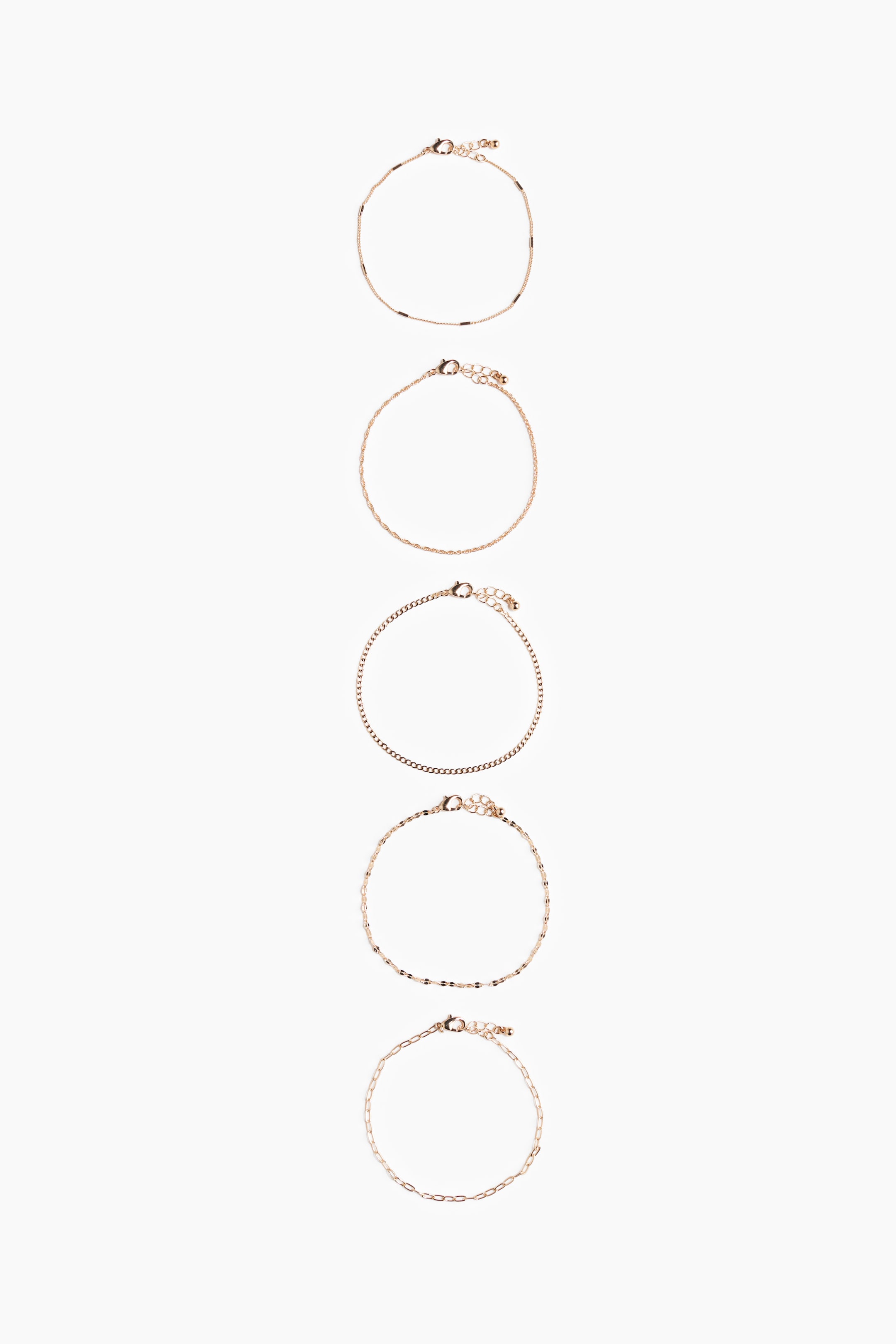 Agrandir l'image: Cinq bracelets dorés sont exposés, chacun présentant un style de chaîne distinct. Ces styles incluent une chaîne délicate avec de petits accents en barre sombre, un design en corde torsadée, une chaîne gourmette classique, une chaîne avec des maillons plats alternés, et une chaîne allongée de type trombone. Chaque bracelet est doté d'un fermoir mousqueton et d'une chaîne d'extension.