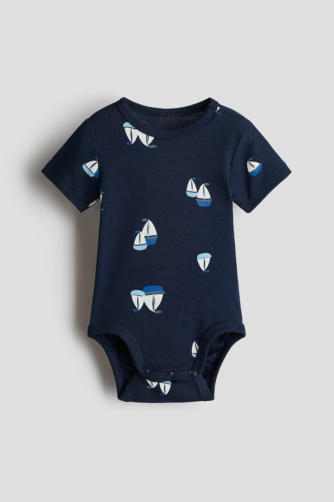 A navy short-sleeved bodysuit, presented FRONT, is made of soft cotton jersey featuring an all-over white and blue sailboat print. It includes a round, trimmed neckline and press-studs on one shoulder and at the bottom. - 1