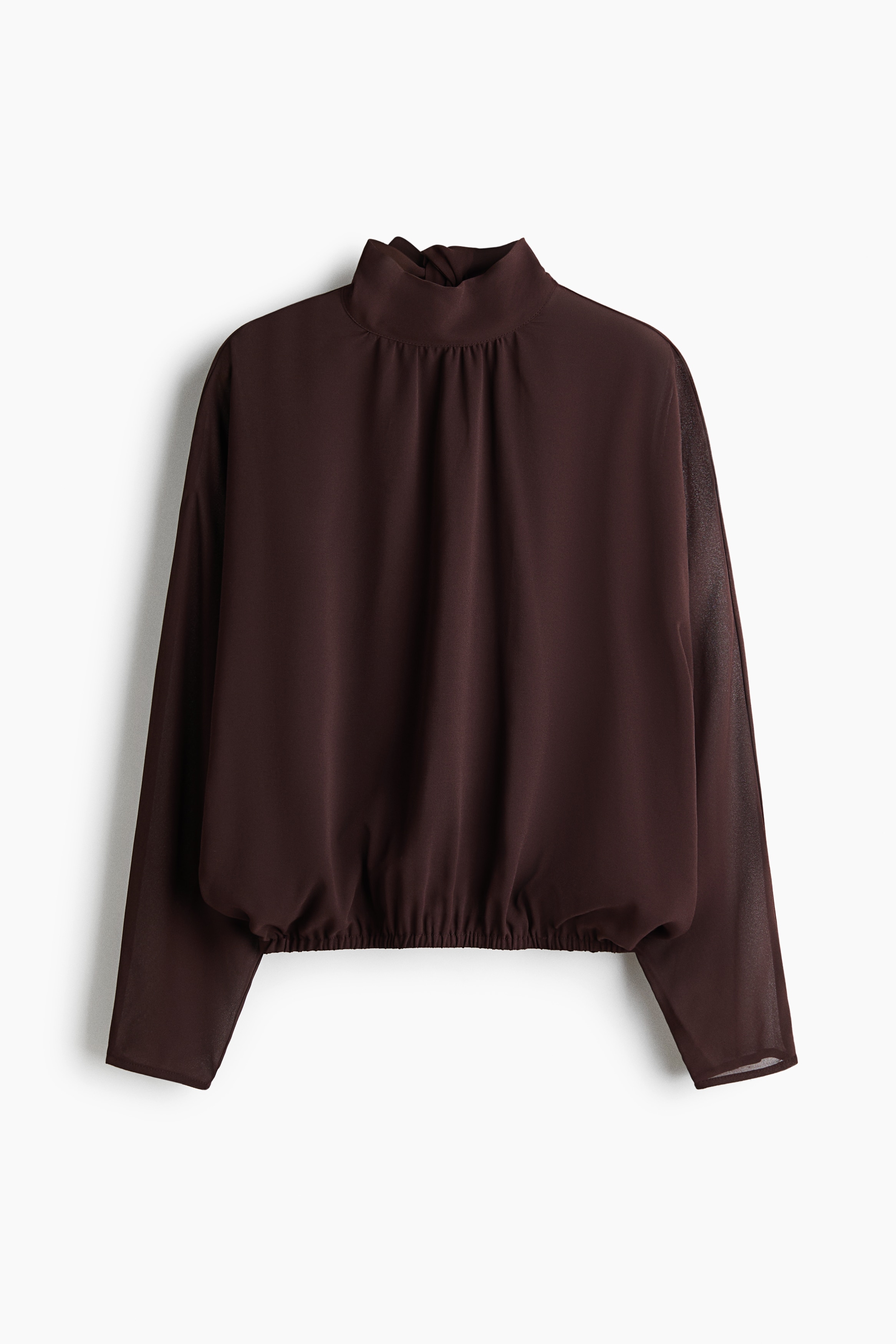 La modelo lleva una blusa marrón oscuro con cuello mao y mangas largas. La blusa ligera y con caÃda presenta un cuello alto fruncido y se combina con pantalones beige de cordón ajustable.