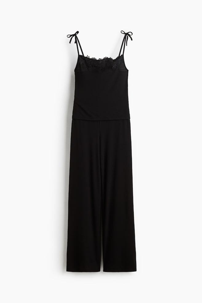 Ein schwarzes geripptes Pyjama-Set liegt flach da, bestehend aus einem Camisole-Top mit einem spitzenbesetzten Ausschnitt und Spaghettiträgern zum Binden sowie dazu passenden Hosen mit weitem Bein. - 1