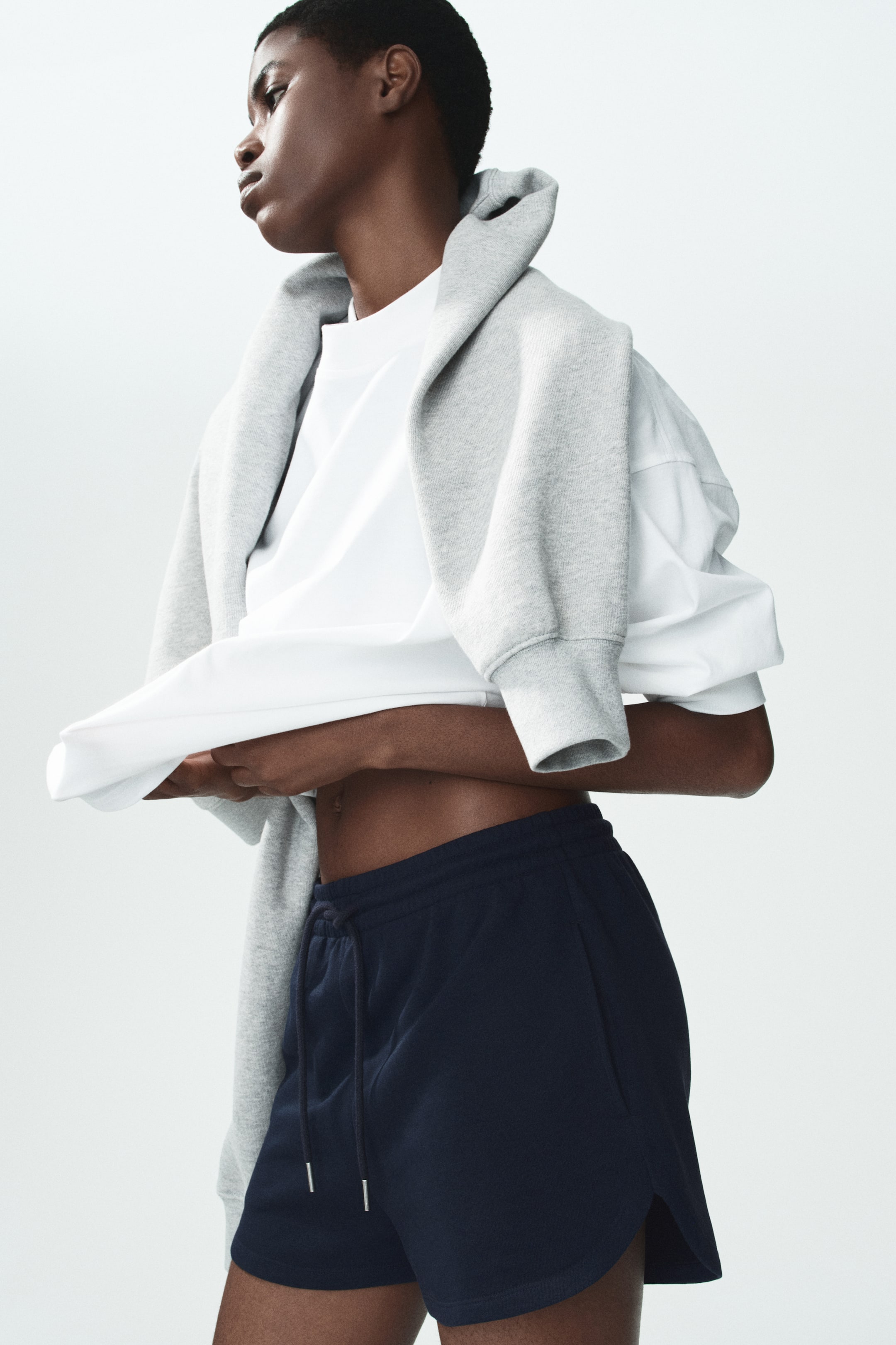 View larger image: The model is wearing navy shorts made from a lightweight sweatshirt fabric. These shorts include a drawstring waistband and a curved hem with side slits.