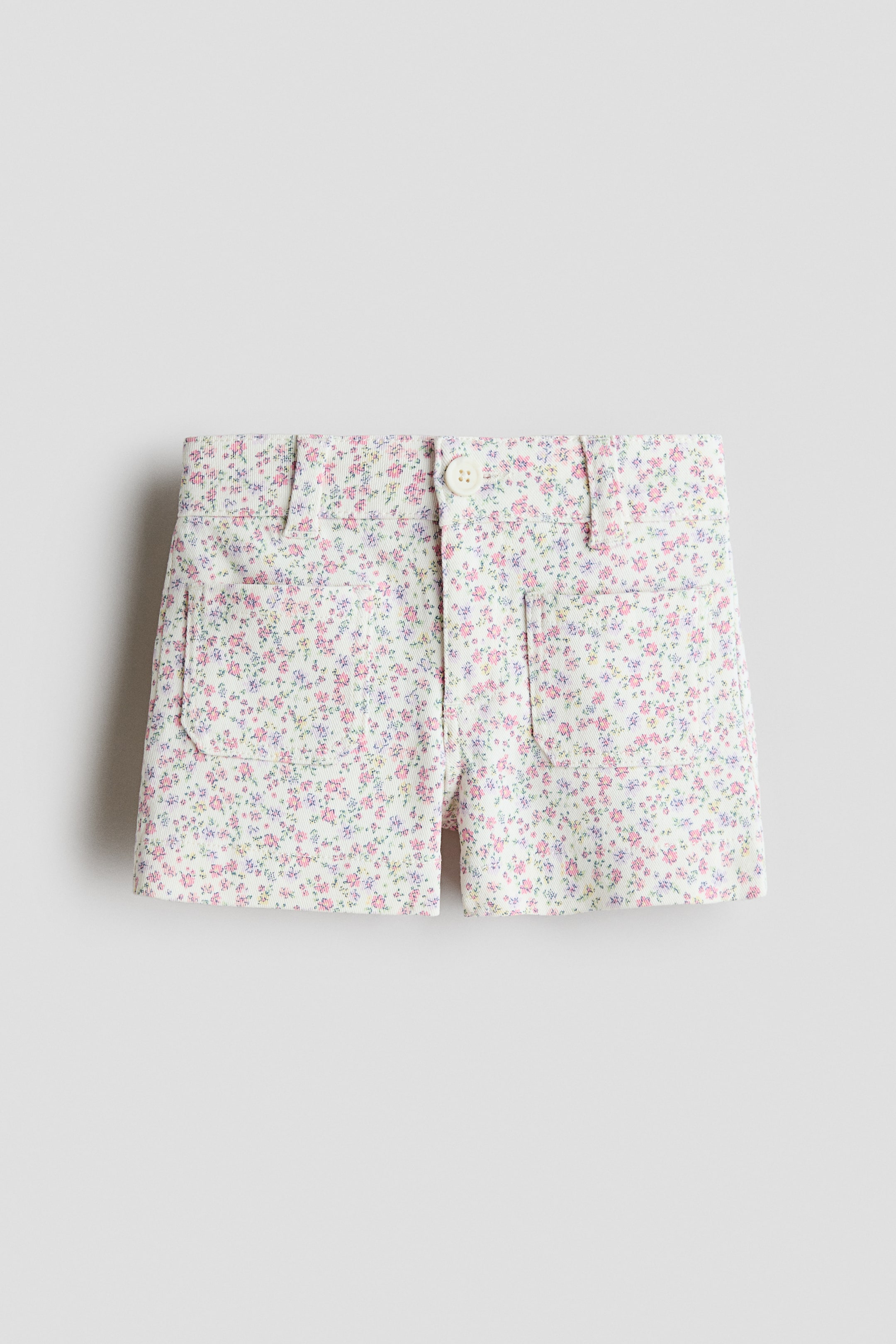 View larger image: The shorts feature a white base with a delicate floral print in pink, purple, and green, shown from a front view. They are designed with a button fastening, belt loops, and two front patch pockets.