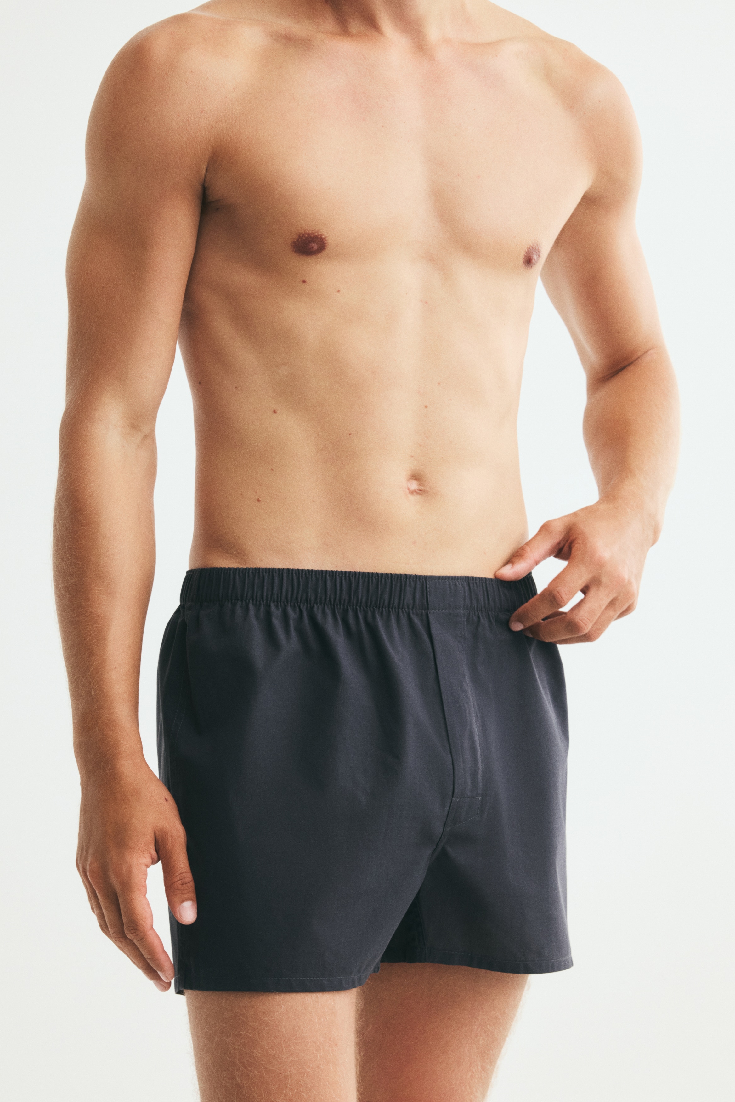 Vier Paar Boxershorts werden in Schichten von Schwarz bis Hellgrau präsentiert, jede mit einem weichen Gewebe, einem elastischen Bund, langen Beinen und einem Knopfverschluss an der Vorderseite.