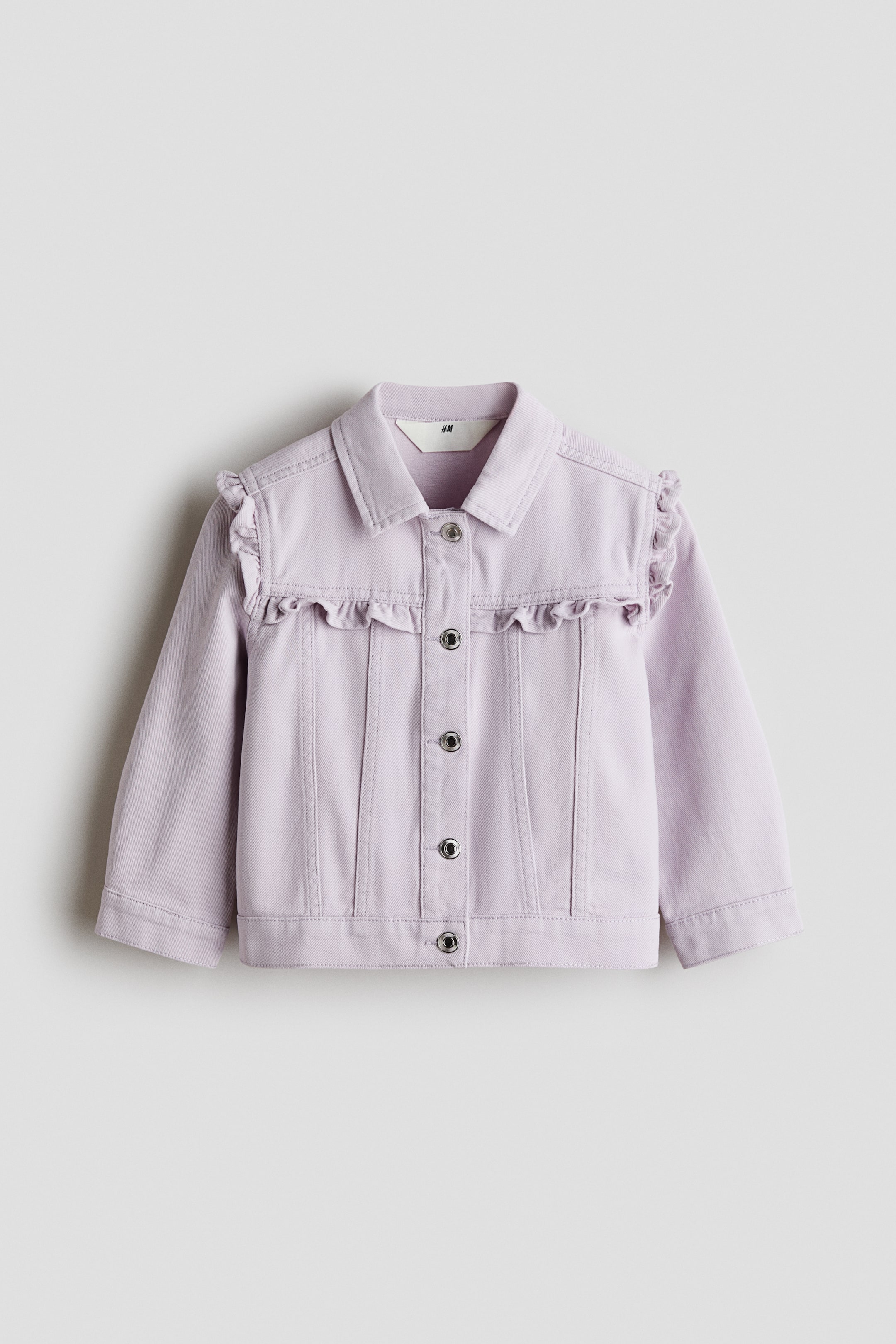 View larger image: A light purple denim jacket featuring a pointed collar, a full snap-button front, and ruffled detailing extending from the shoulders across the chest yoke.