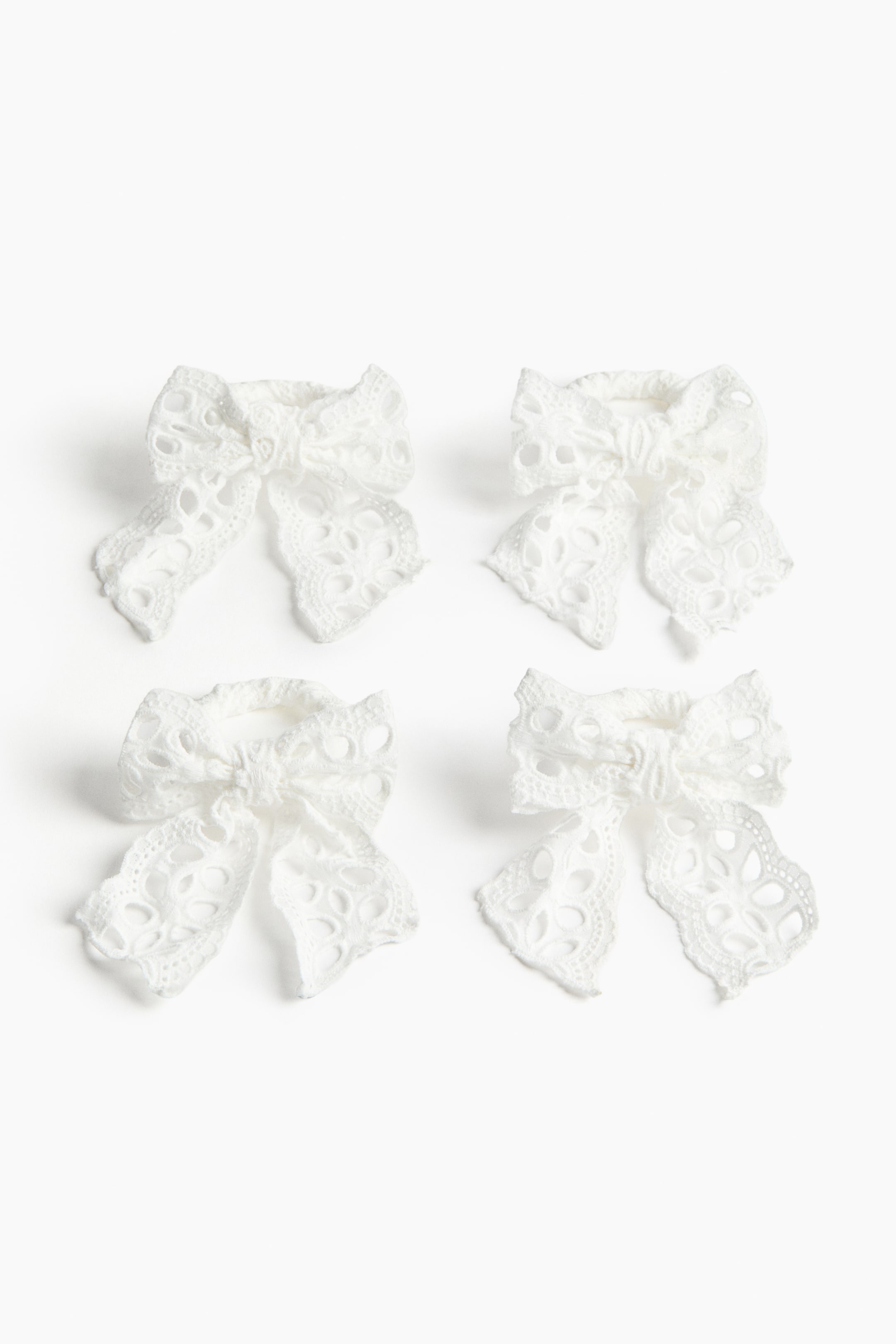 View larger image: Four white eyelet bows are displayed. Each bow features two loops and two tails, with the entire fabric showcasing intricate embroidered cut-out detailing.