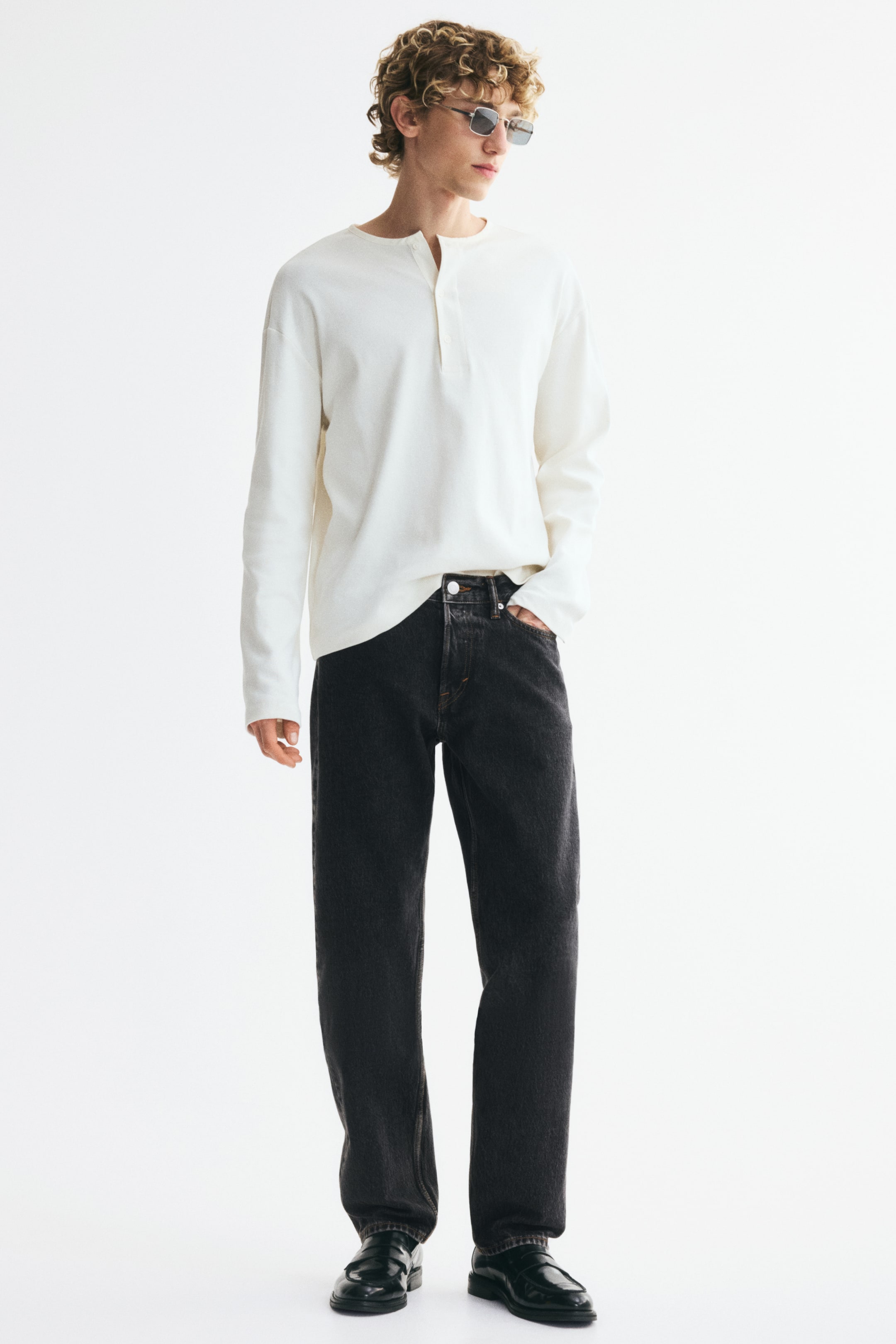 View larger image: Five-pocket jeans in dark gray rigid cotton denim feature a regular waist with a visible button fly, and a straight leg with a comfortable, looser fit from the waist to the hem. The model is wearing the jeans, with one hand resting in a front pocket.