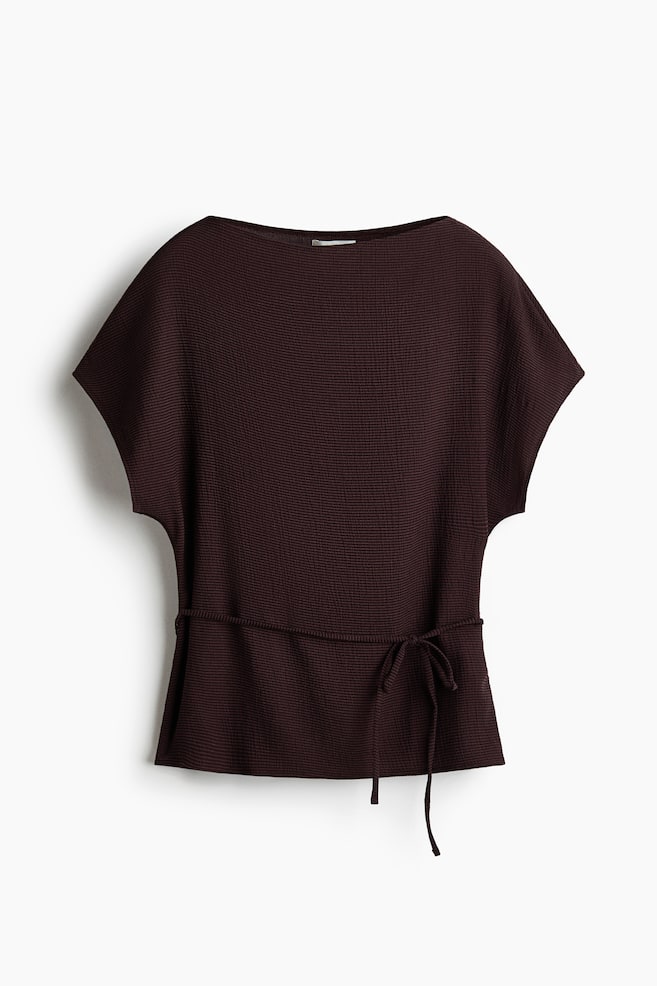 A dark brown textured jersey top is shown from the front, featuring a boat neckline, short batwing sleeves and a narrow tie belt at the waist. The garment showcases a fine, crinkled texture throughout its relaxed silhouette. - 1
