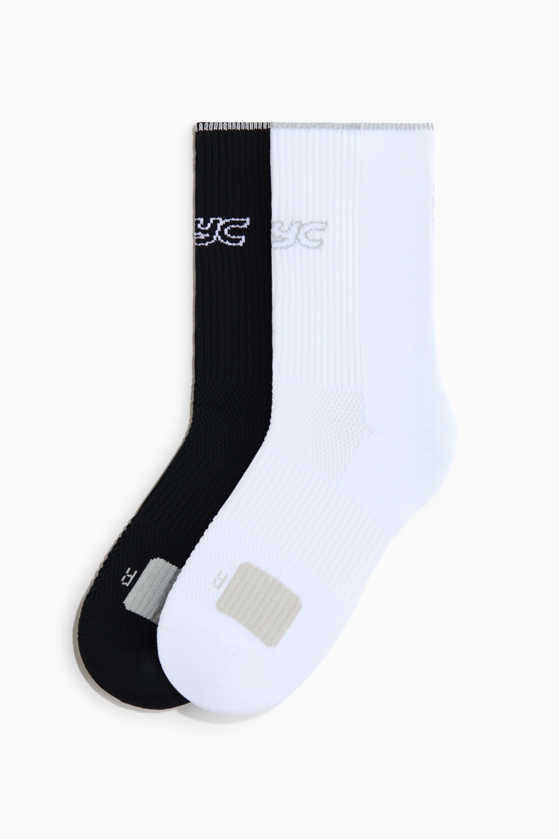 View larger image: A pair of crew socks, featuring one black and one white sock, is laid flat with the white sock partially overlapping the black one. Both socks feature ribbed cuffs with a stylised logo, a ribbed arch band, and a grey rectangular patch on the forefoot marked with the letter “R”.