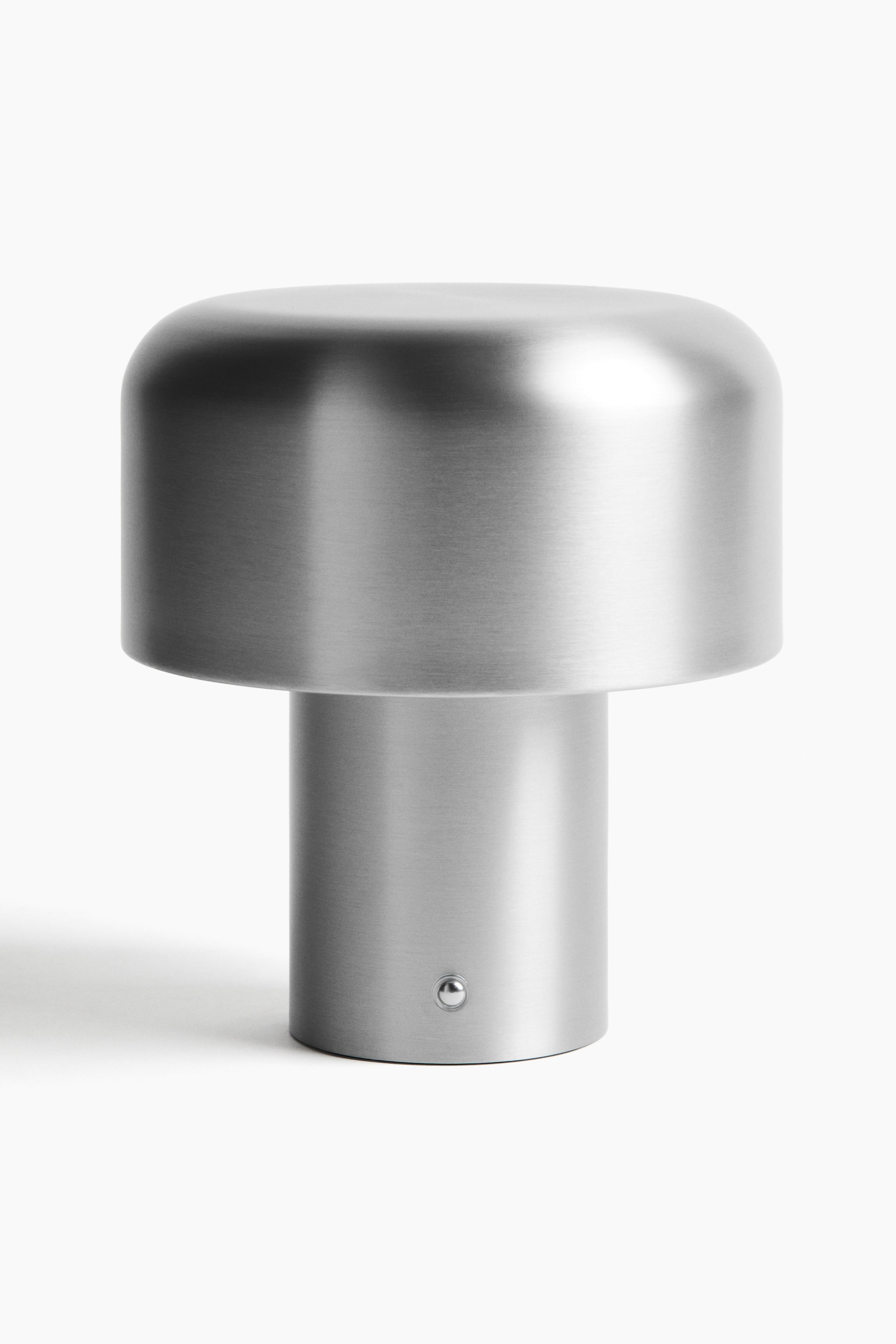 Grösseres Bild ansehen: Ein silbernes, gebürstetes Metallobjekt verfügt über eine zylindrische Basis, aus der ein schmalerer, zylindrischer Schaft nach oben ragt und ein breiteres, abgerundetes Oberteil trägt. Auf der Vorderseite der Basis ist ein kleiner, runder, silberner Knopf sichtbar.