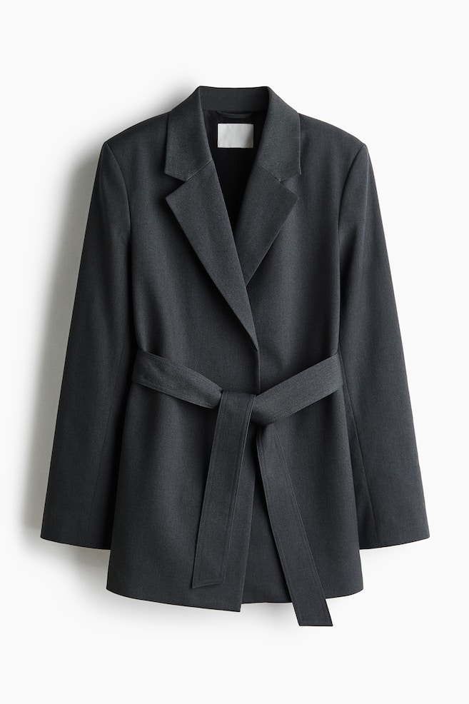 A dark grey woven blazer is shown from the front, featuring structured shoulders, prominent notch lapels, and a matching fabric tie belt securing the open front at the waist. - 1