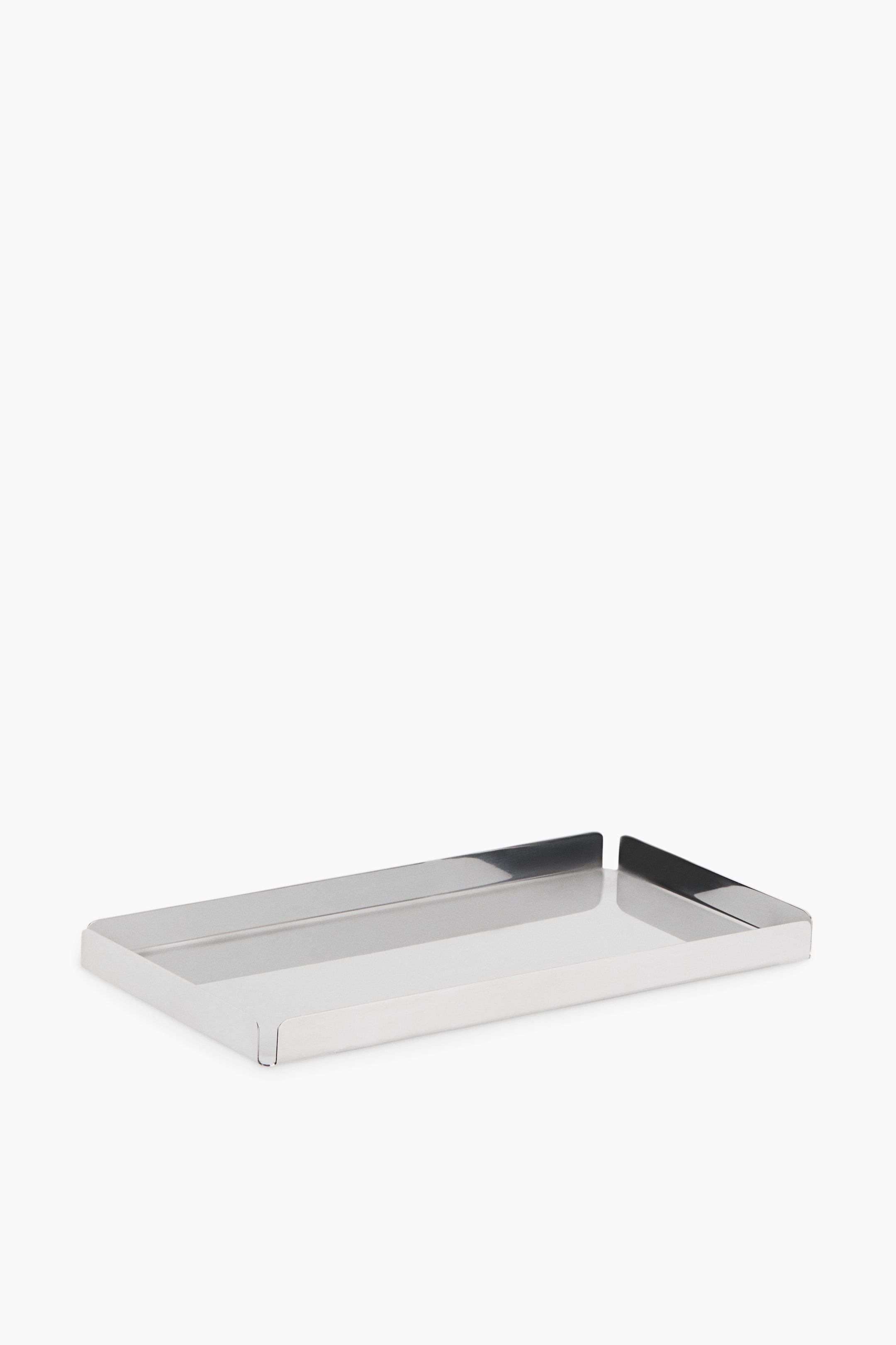 View larger image: A rectangular metal tray is displayed from a front three-quarter angle, showing a highly polished, reflective silver finish. It features low, straight raised edges with distinct folded-corner details that leave small open gaps.