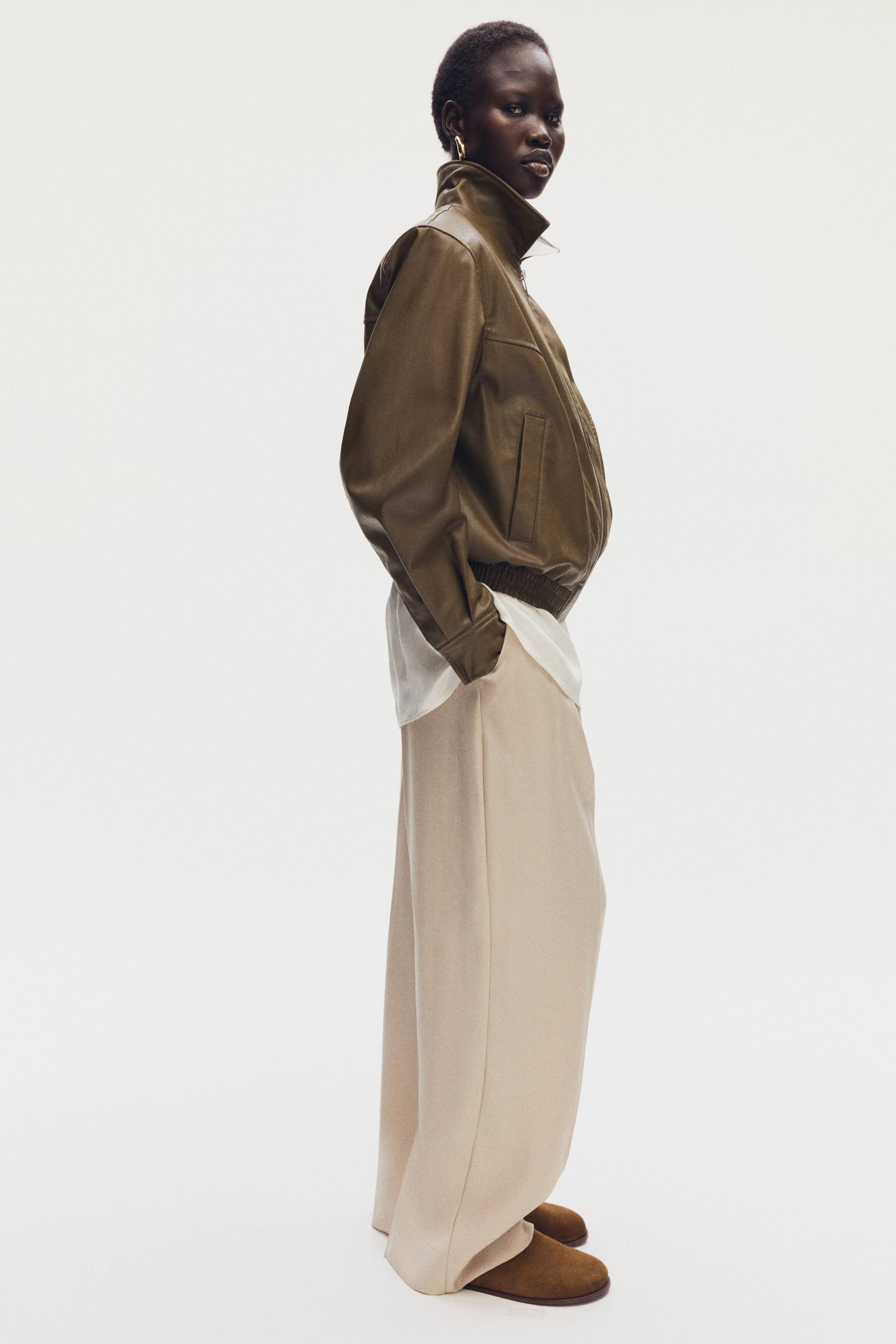 Ampliar la imagen: Mules de gamuza marrón suave con puntas oblicuas están siendo usados por la modelo, parcialmente cubiertos por pantalones de pierna ancha de color claro.