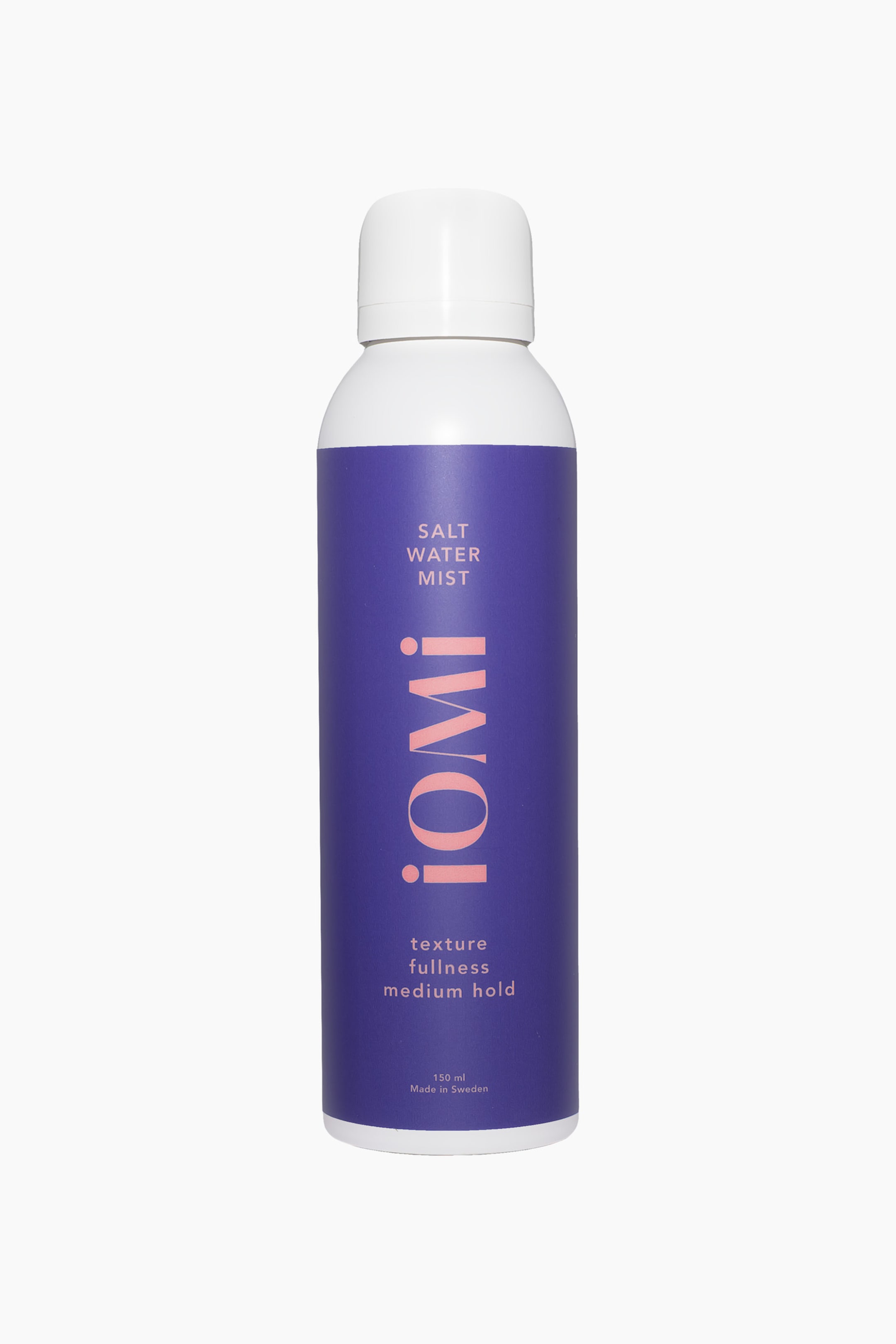 Se større billede: En hvid cylindrisk sprayflaske med en hvid hætte står oprejst og vender fremad. En lilla etiket omslutter flasken, med "SALT WATER MIST" i hvid tekst, "iOMi" i lyserøde bogstaver vertikalt, og "texture fullness medium hold" i hvid tekst.