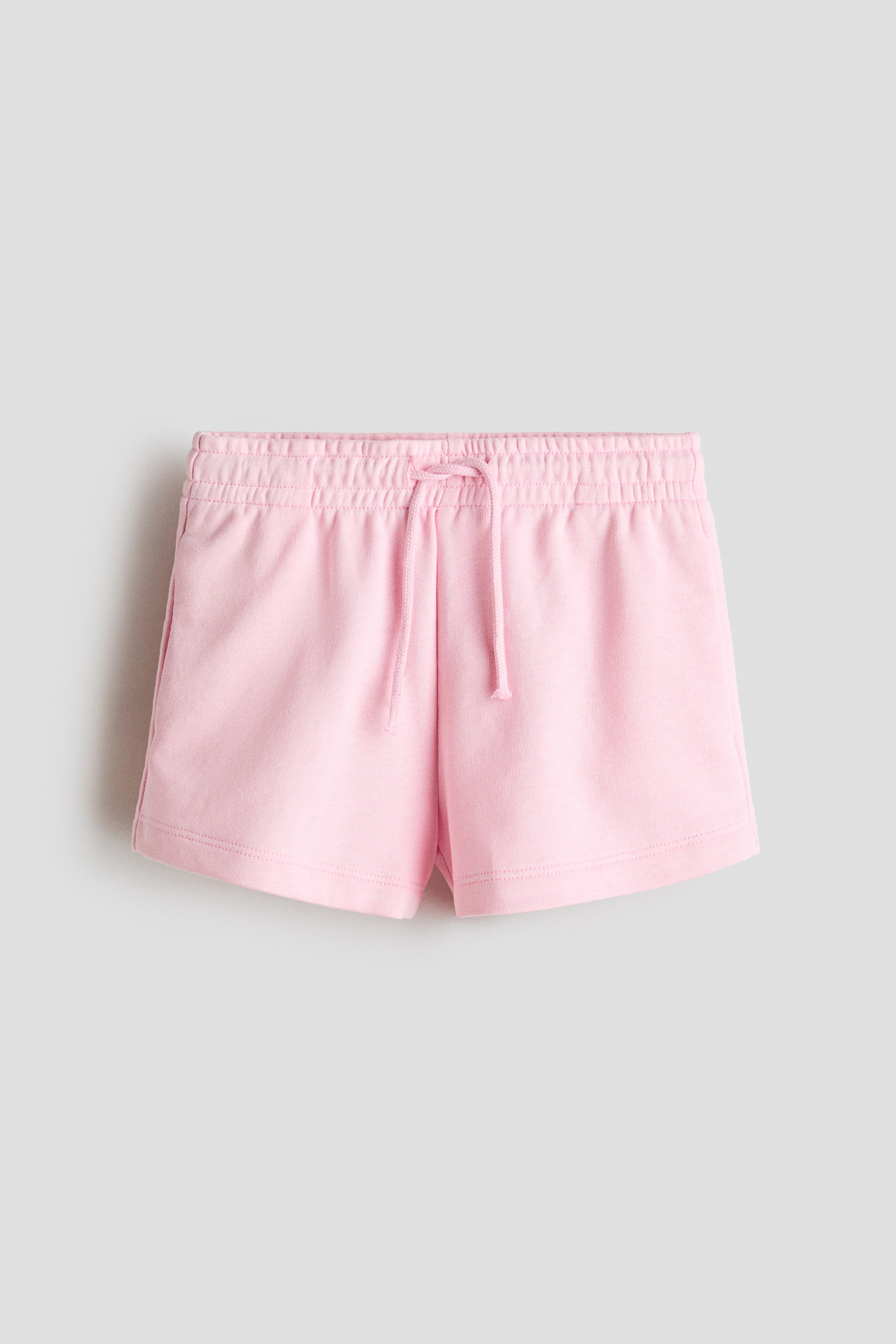 View larger image: Pink shorts feature a lightweight sweatshirt fabric, an elastic drawstring waist with a tied cord, and discreet side pockets. They are shown from the front.