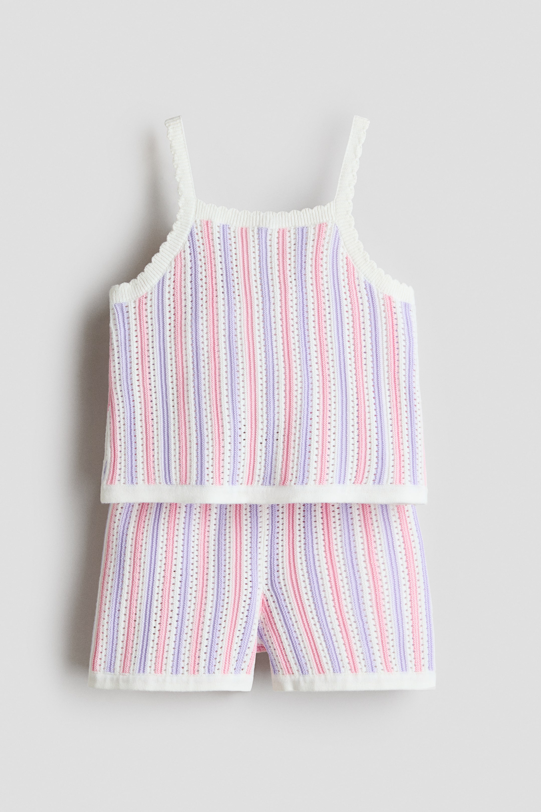 Prikaži veću sliku: Komplet od dva dela, koji se sastoji od topa sa bretelama i šortsa, prikazan je sa prednje strane. Oba dela su izrađena od tkanine sa teksturom i vertikalnim prugama u beloj, roze i svetlo ljubičastoj boji, sa ivicama u obliku školjke na bretelama, izrezu, otvorima za ruke i porubima.