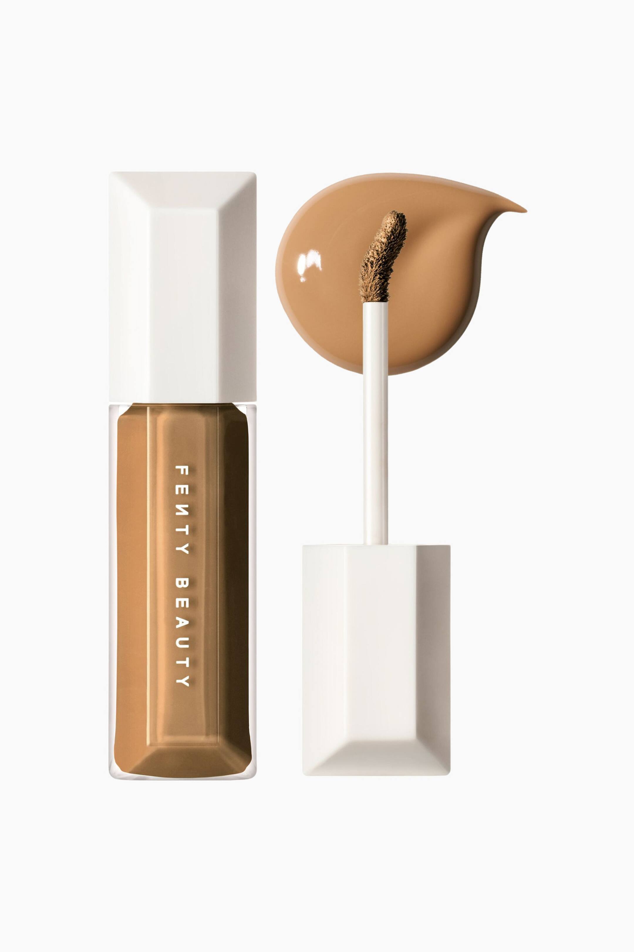 Visa större bild: We're Even Hydrating Longwear Concealer visas i en tydlig, facetterad rektangulär flaska fylld med en medelbrun vätska, med ett vitt facetterat lock och vertikal branding. Intill flaskan står den matchande applikatorstaven upprätt och visar sin böjda, produktbelagda spets placerad mot en slät, droppformad swatch i samma concealer-nyans.