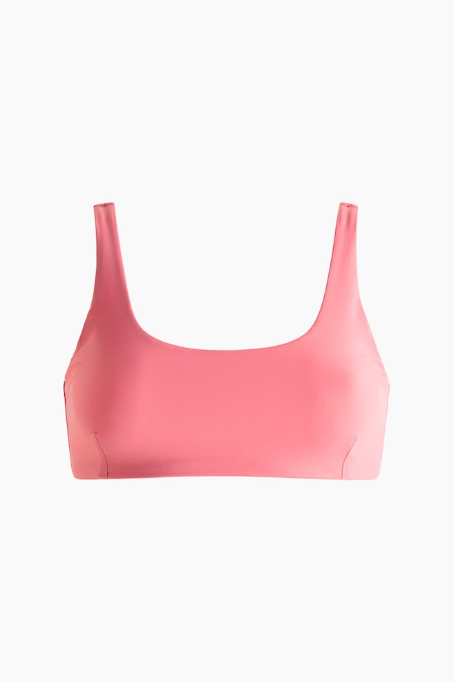 A pink swim top is showcased from the front. It features a scoop neckline and wide shoulder straps, with subtle vertical seams visible on each side just above the bottom band. - 1