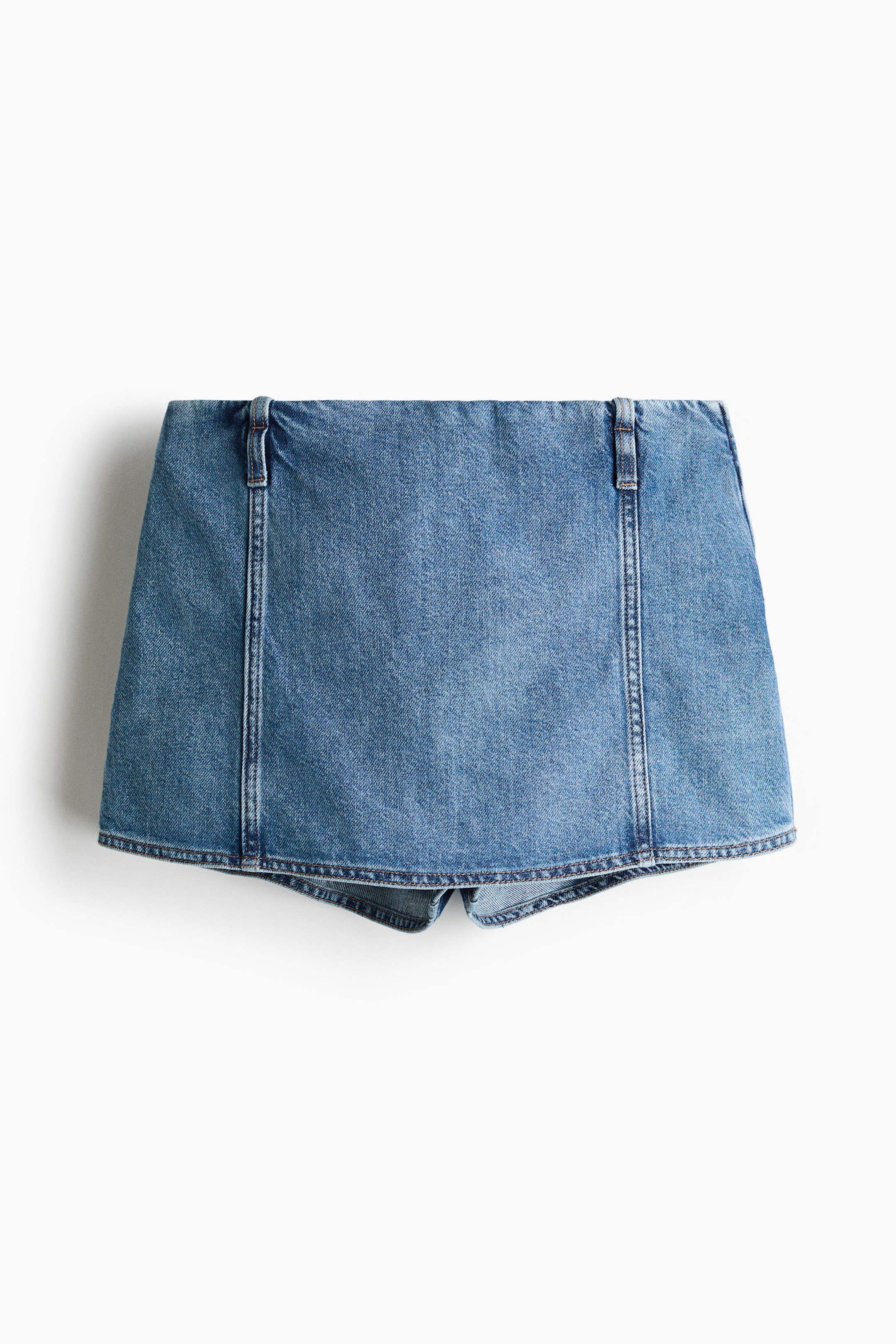 View larger image: A short skort in rigid blue cotton denim is shown from the back. It features vertical seams on the back and small belt loops at the waist.
