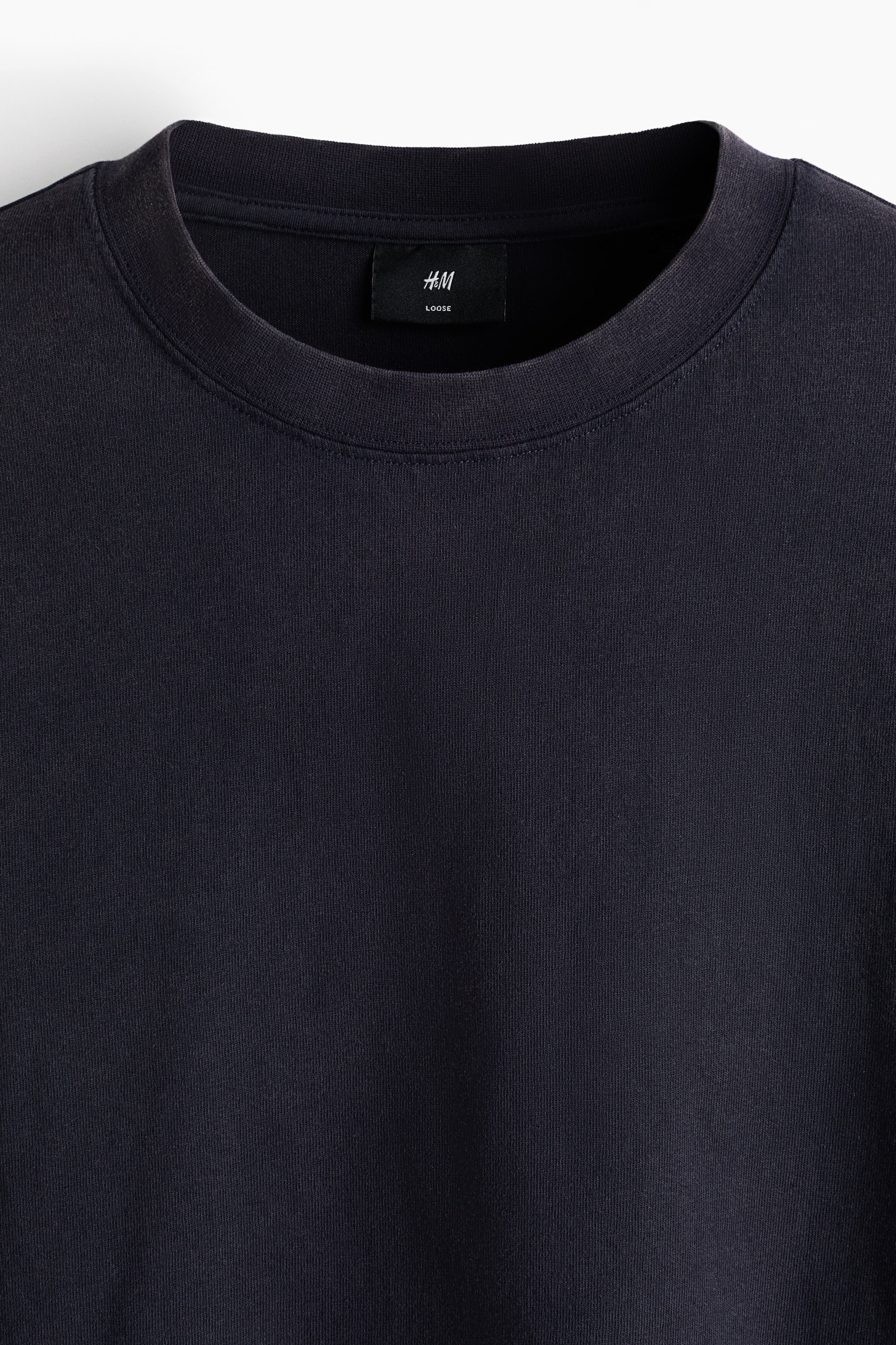 Größeres Bild anzeigen: Ein verwaschenes schwarzes Rundhals-T-Shirt zeigt seine Vorderseite. Es verfügt über einen gerippten Kragen und ein innenliegendes schwarzes Etikett mit der weißen Aufschrift „H&M LOOSE“.