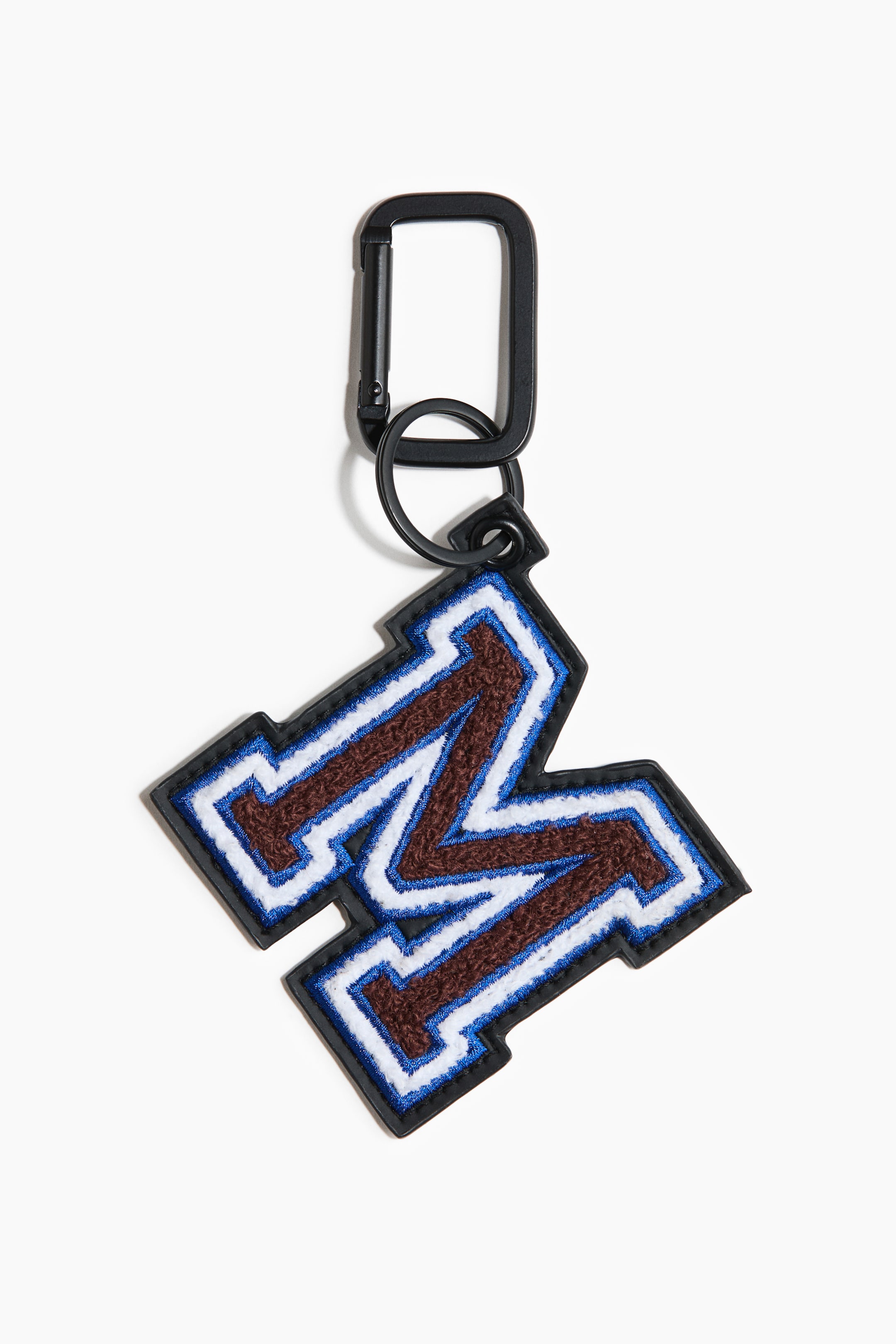 View larger image: A bag charm featuring a black carabiner clip and a black split ring. The charm is an embroidered varsity-style letter M, showcasing brown chenille with white and blue outlines, all bordered in black.