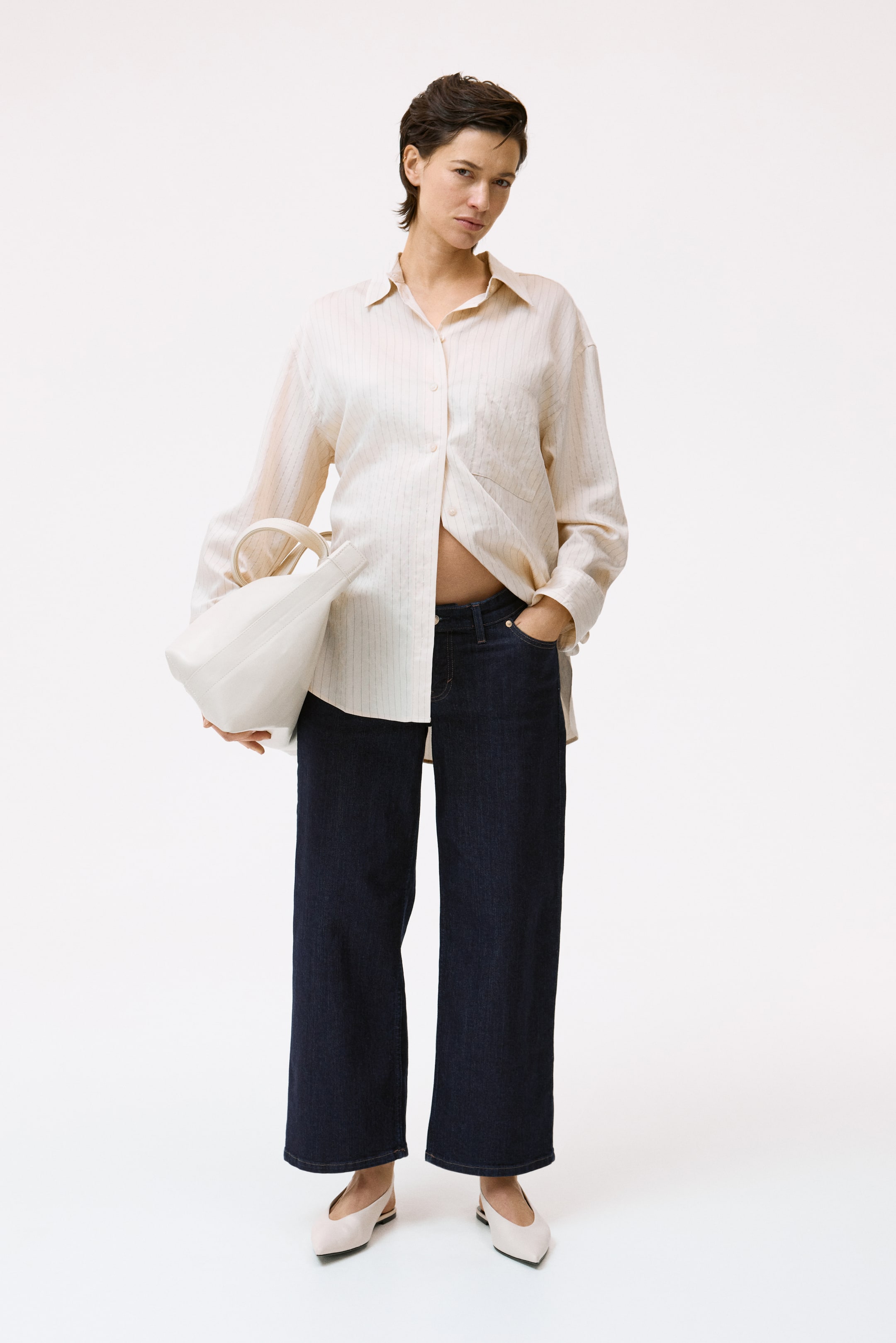View larger image: Shirt: An oversized beige button-down shirt features subtle vertical stripes and a standard collar. It's styled untucked over dark jeans, with the lower buttons partially undone.