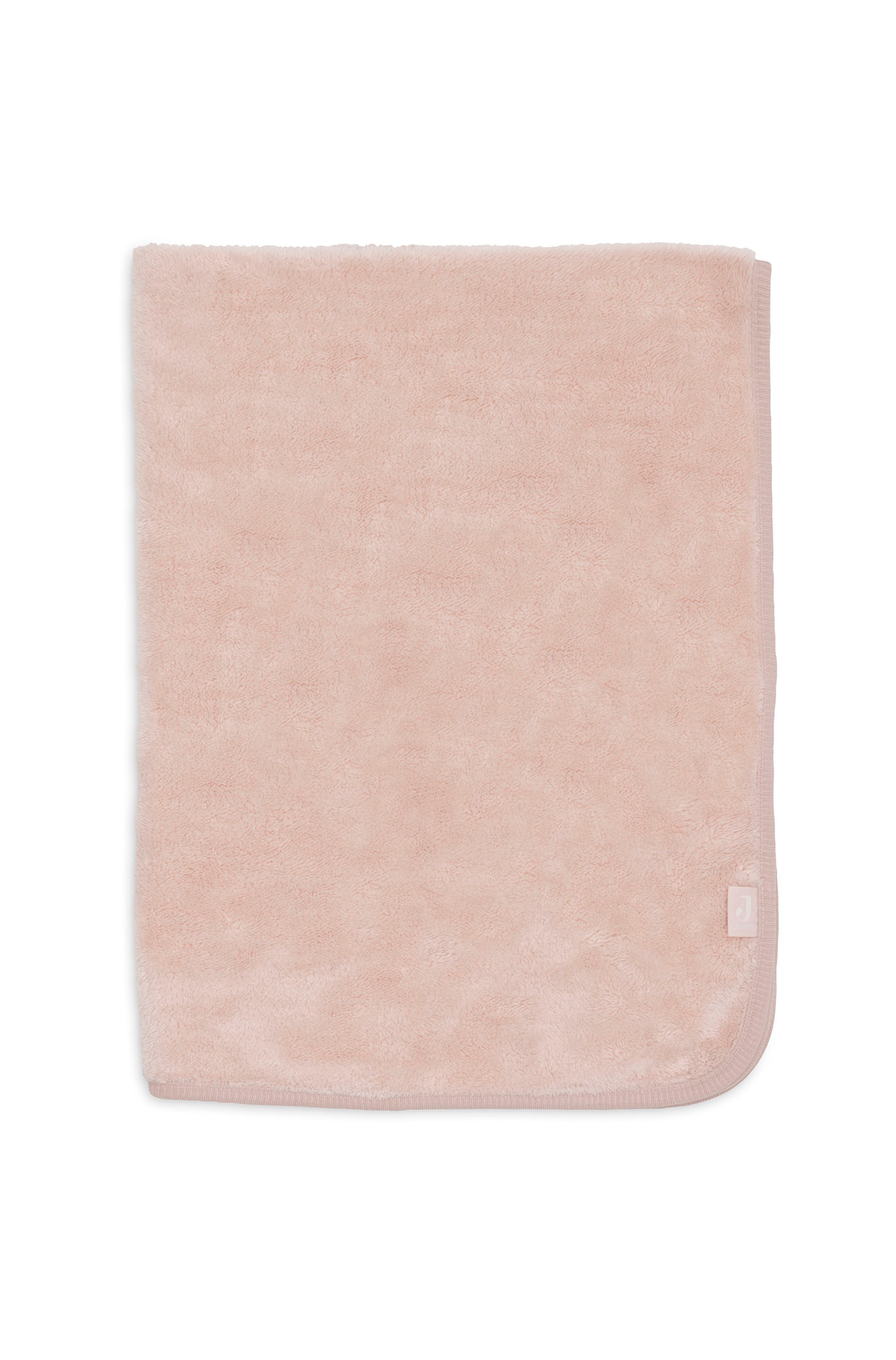 Agrandir l'image: Une couverture moelleuse rose poudré est posée à plat, pliée en forme rectangulaire, mettant en valeur sa surface en polaire douce et texturée. La couverture présente une bordure en tissu lisse le long des bords inférieur et droit, avec une petite étiquette logo blanche fixée près du coin inférieur droit.