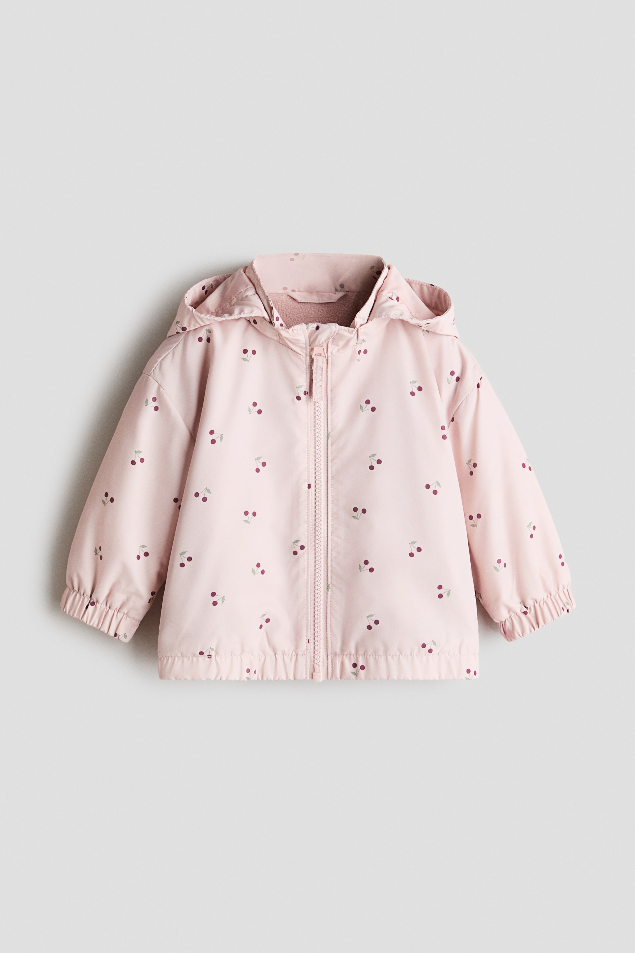 View larger image: A light pink jacket with an all-over cherry print is showcased from the front, featuring a hood, a stand collar, a full-length zipper, and covered elastication at the cuffs and hem.