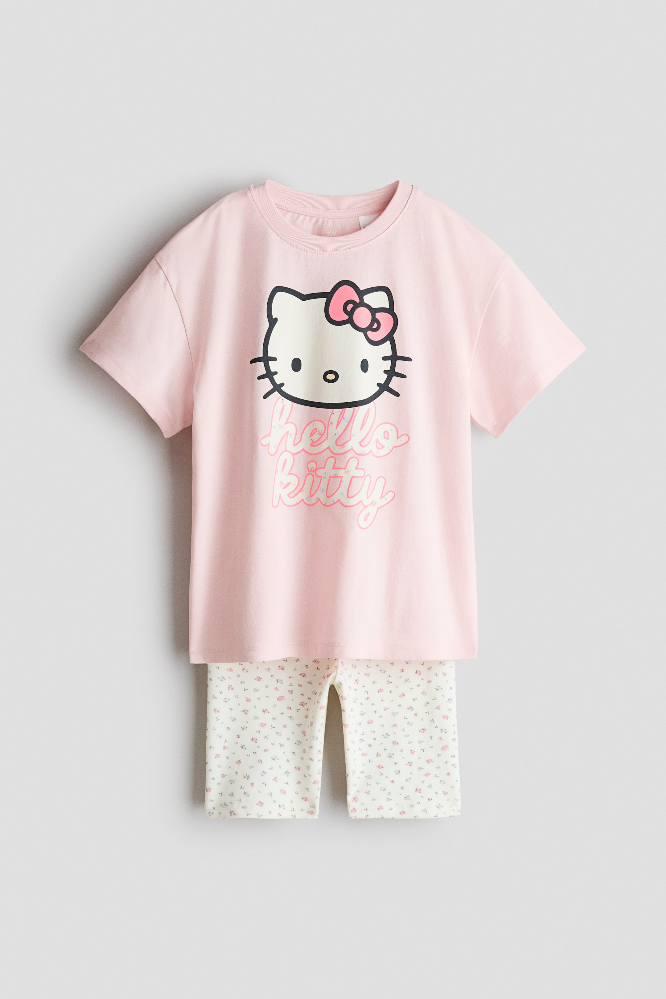 Voir une image plus grande: Un ensemble imprimé comprenant un t-shirt rose avec un col côtelé et des épaules tombantes, arborant un motif Hello Kitty à l'avant. Il est assorti à un short cycliste blanc cassé, orné d'un petit imprimé floral et doté d'une taille élastiquée.