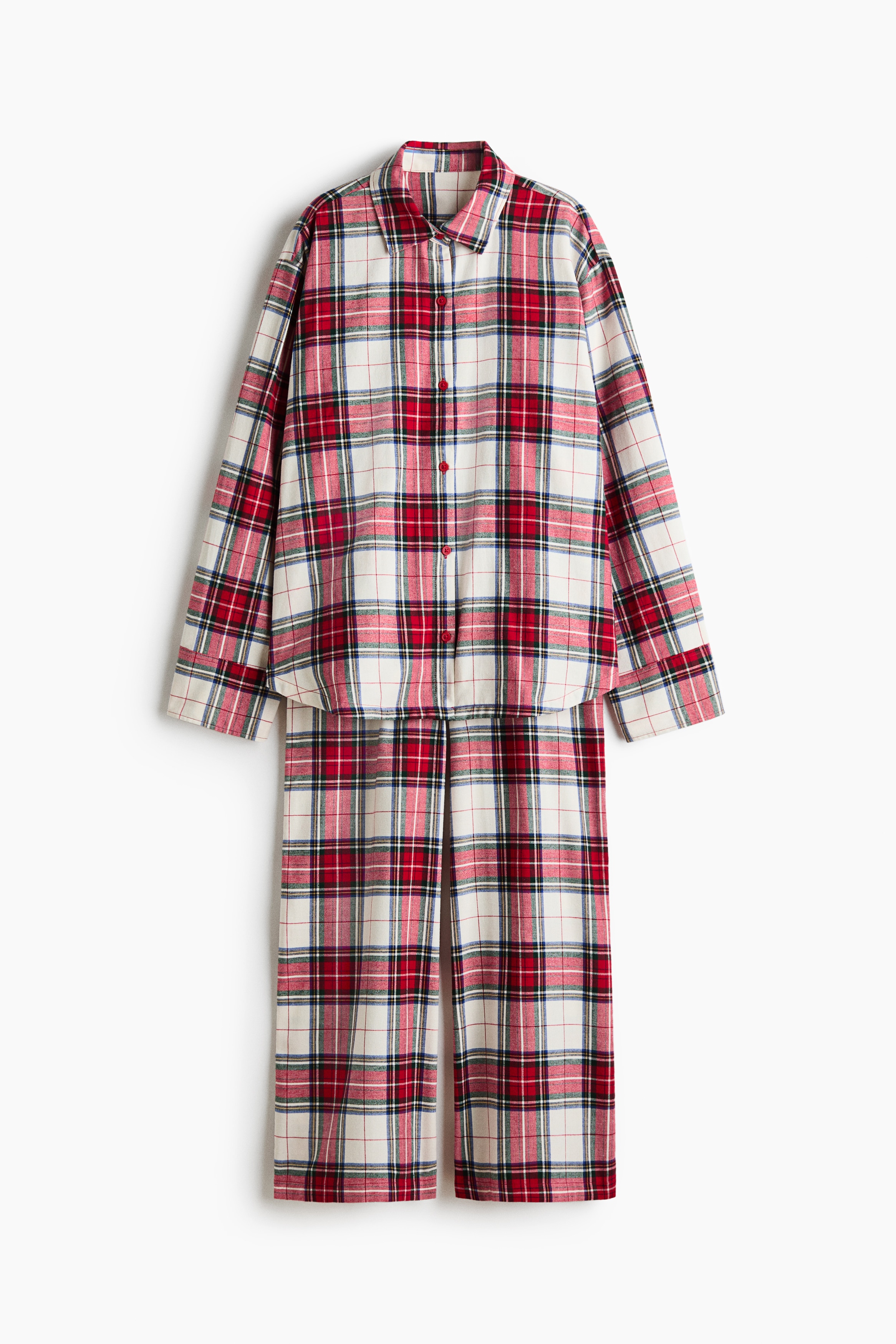 A red, white and black plaid cotton flannel pyjama set is worn by the model sitting on the floor. The long-sleeved shirt is styled open over a white bralette, and the matching wide-leg pants are paired with light beige slippers.