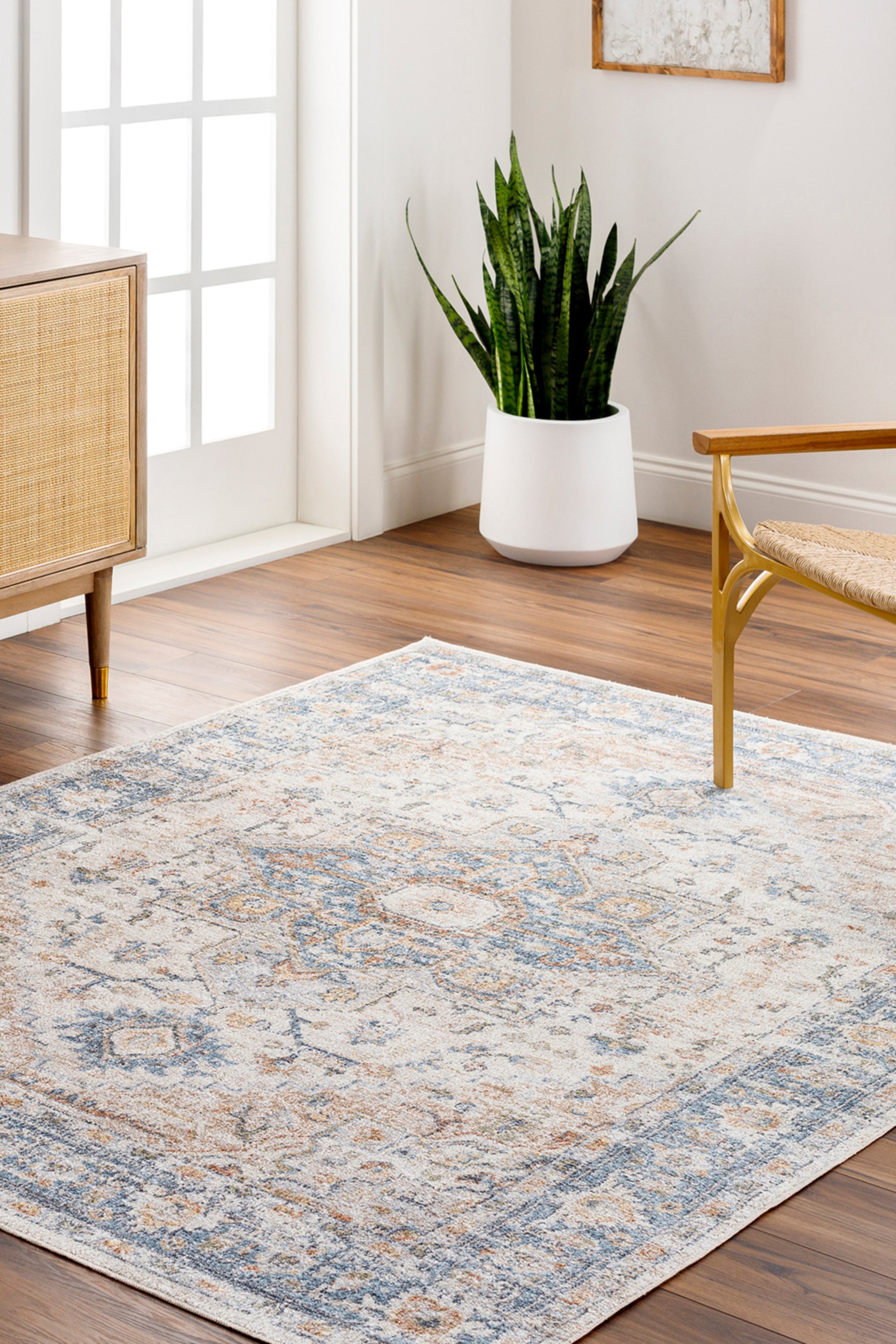 View larger image: A rectangular area rug is lying flat, angled from the bottom left to the top right, showcasing a distressed vintage pattern in cream, blue, and orange tones. It features a central medallion design and a patterned border.