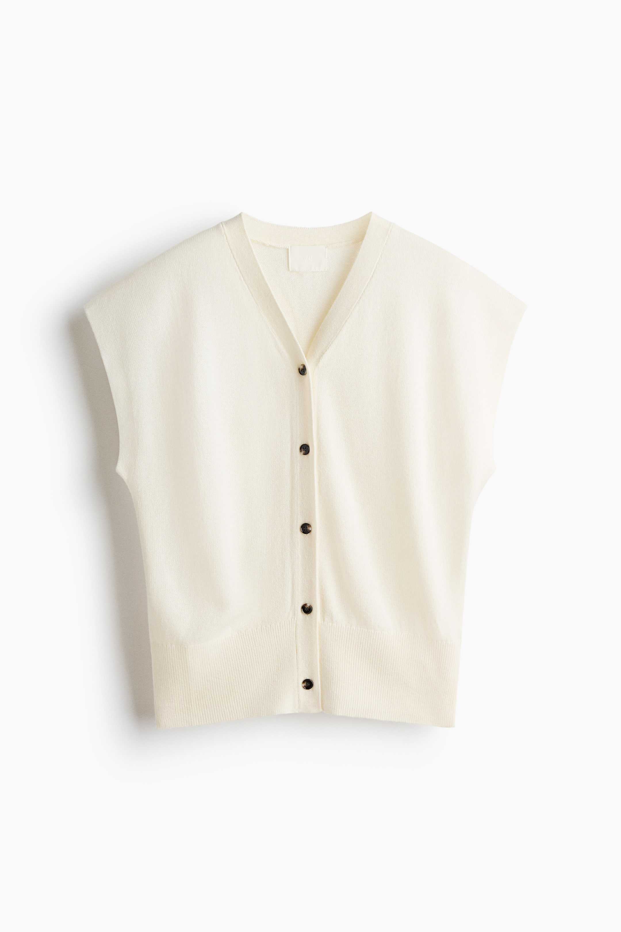 View larger image: A cream sleeveless cardigan is showcasing its front. It features a V-neckline, a button-front closure with five dark buttons, and a ribbed hem.