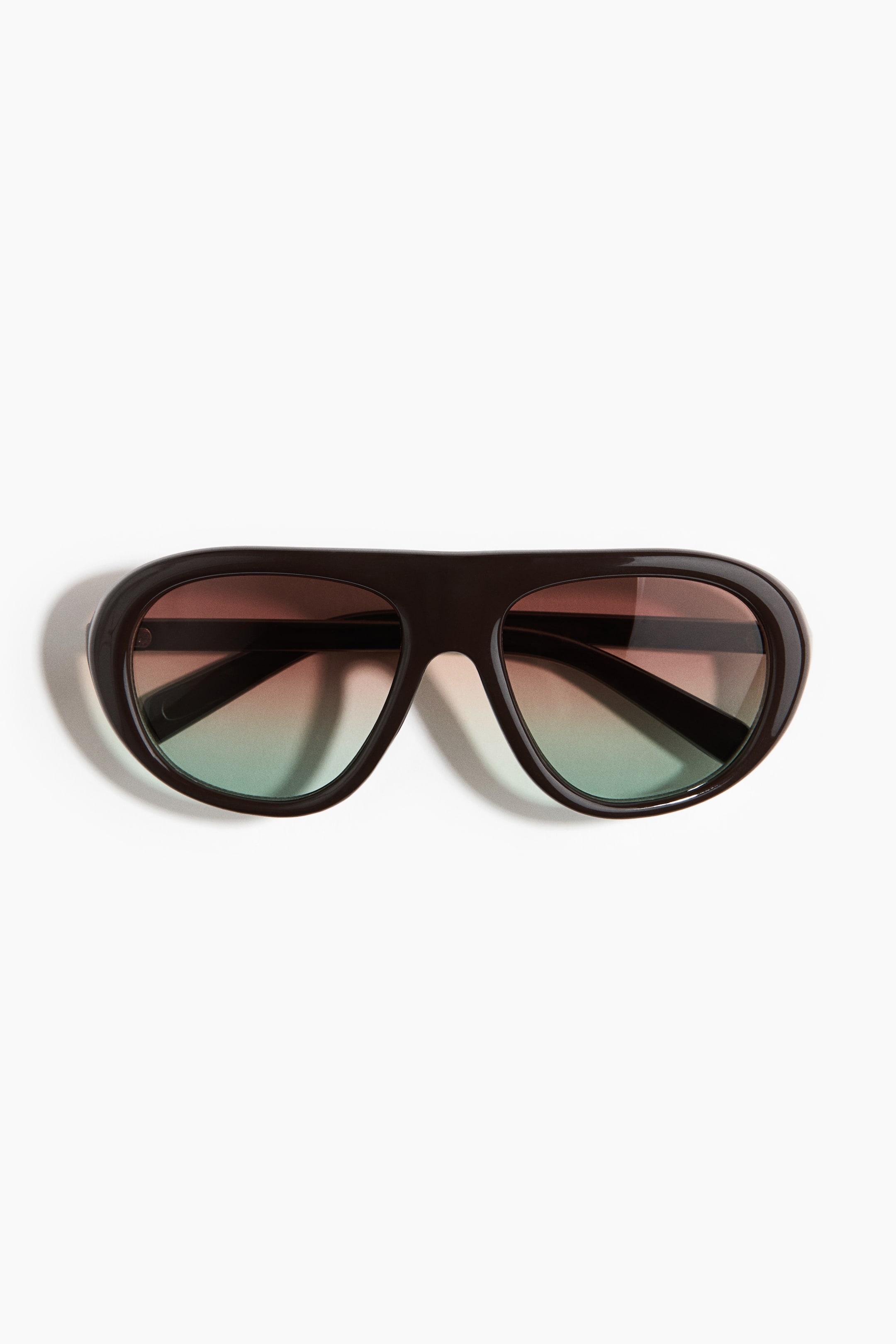 View larger image: Visor sunglasses are displayed from a frontal perspective, showcasing dark plastic frames and side arms. The oversized, tinted plastic lenses exhibit a gradient transitioning from a reddish-brown hue at the top to a green shade at the bottom.